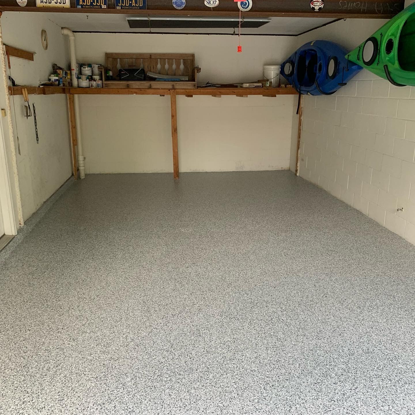 Empty garage with speckled floor, shelves along the back wall, and colorful kayaks stored high on the right.