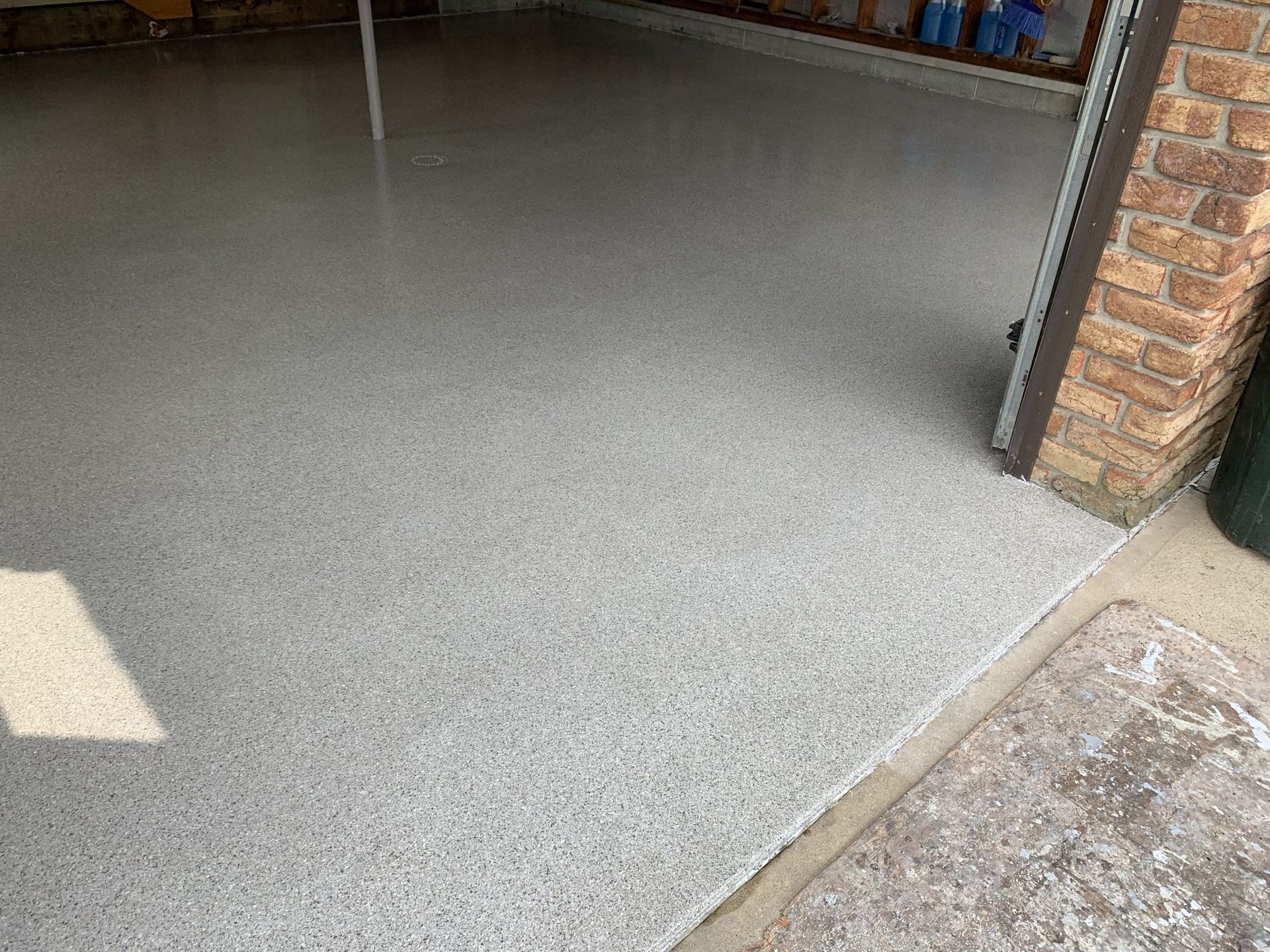 Gray speckled garage floor with a brick wall and open doorway on the right
