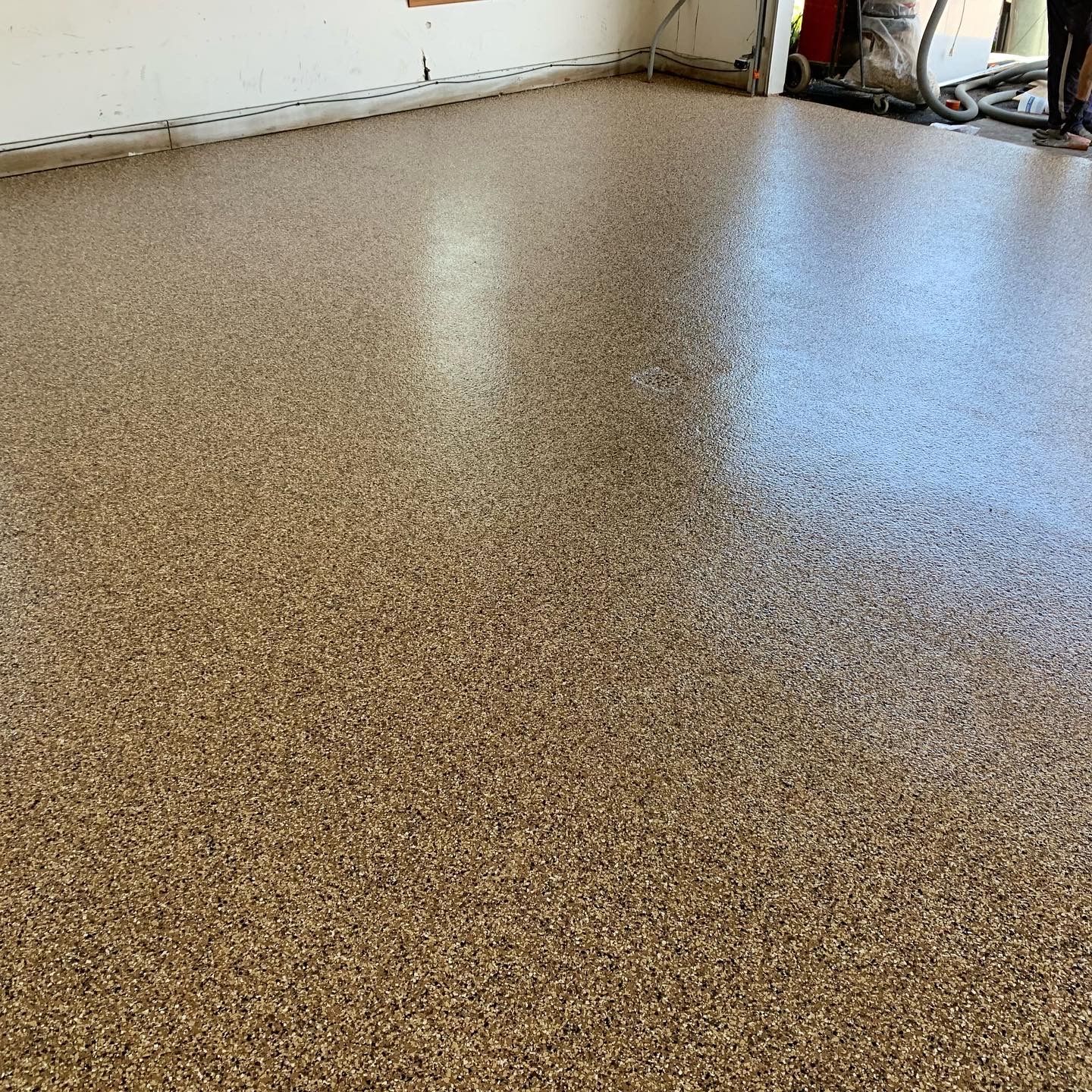 Speckled epoxy floor in a garage, tan with brown flecks and a glossy finish