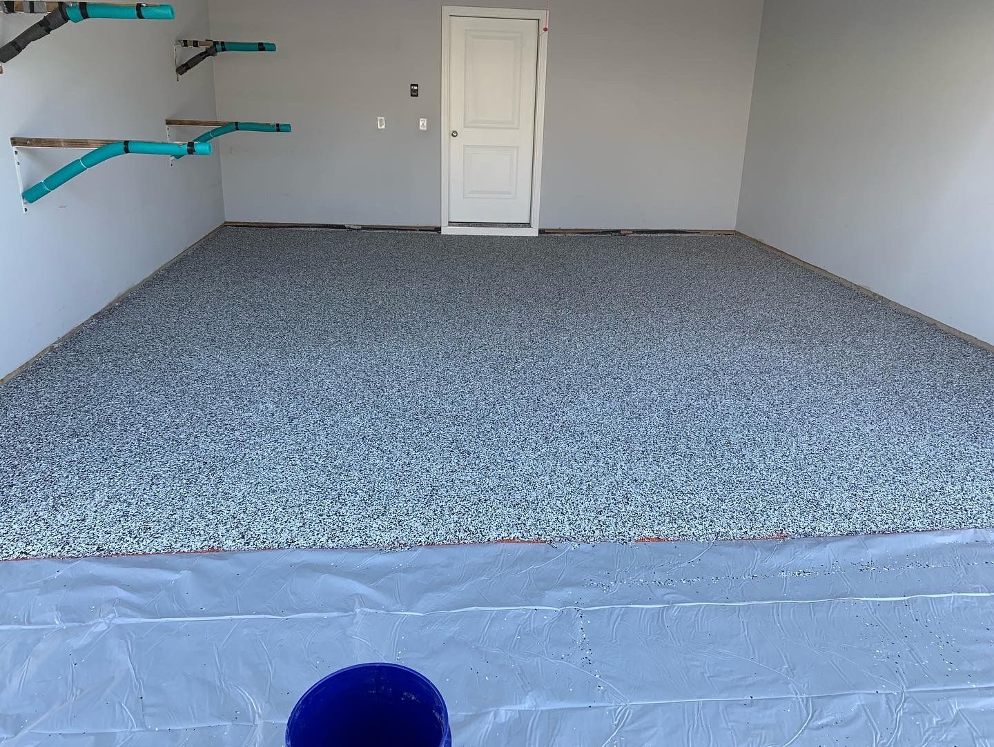 Empty garage with gray carpet, blue wall shelves, and a white door at the back.