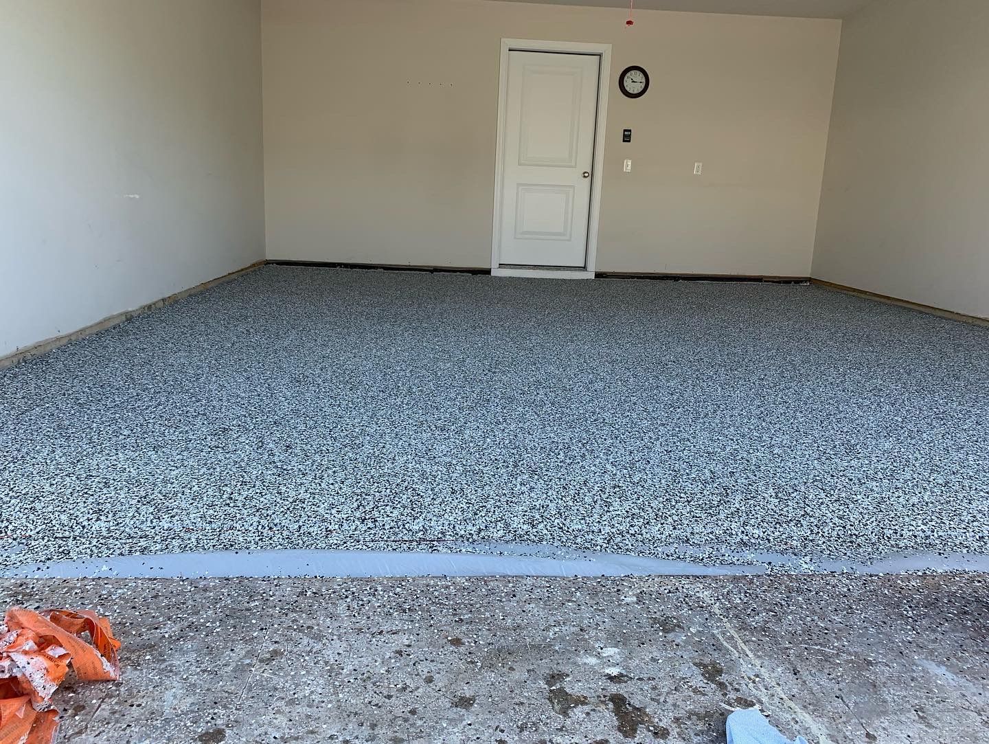 Empty garage interior with gray speckled floor and a white door on the back wall.