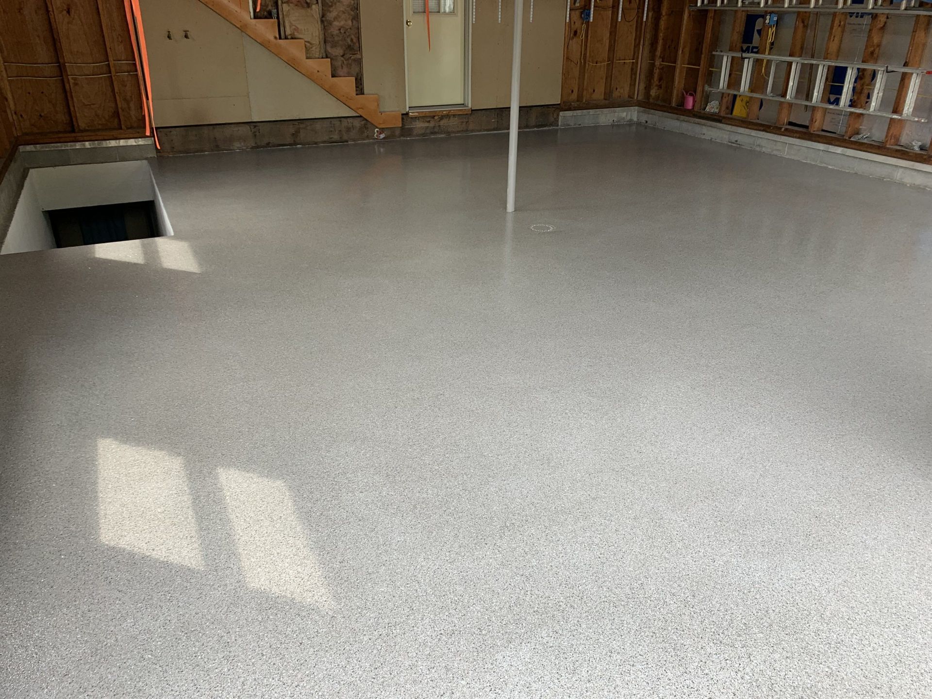 Empty unfinished room with gray concrete floor, exposed studs, and a staircase in the back left.