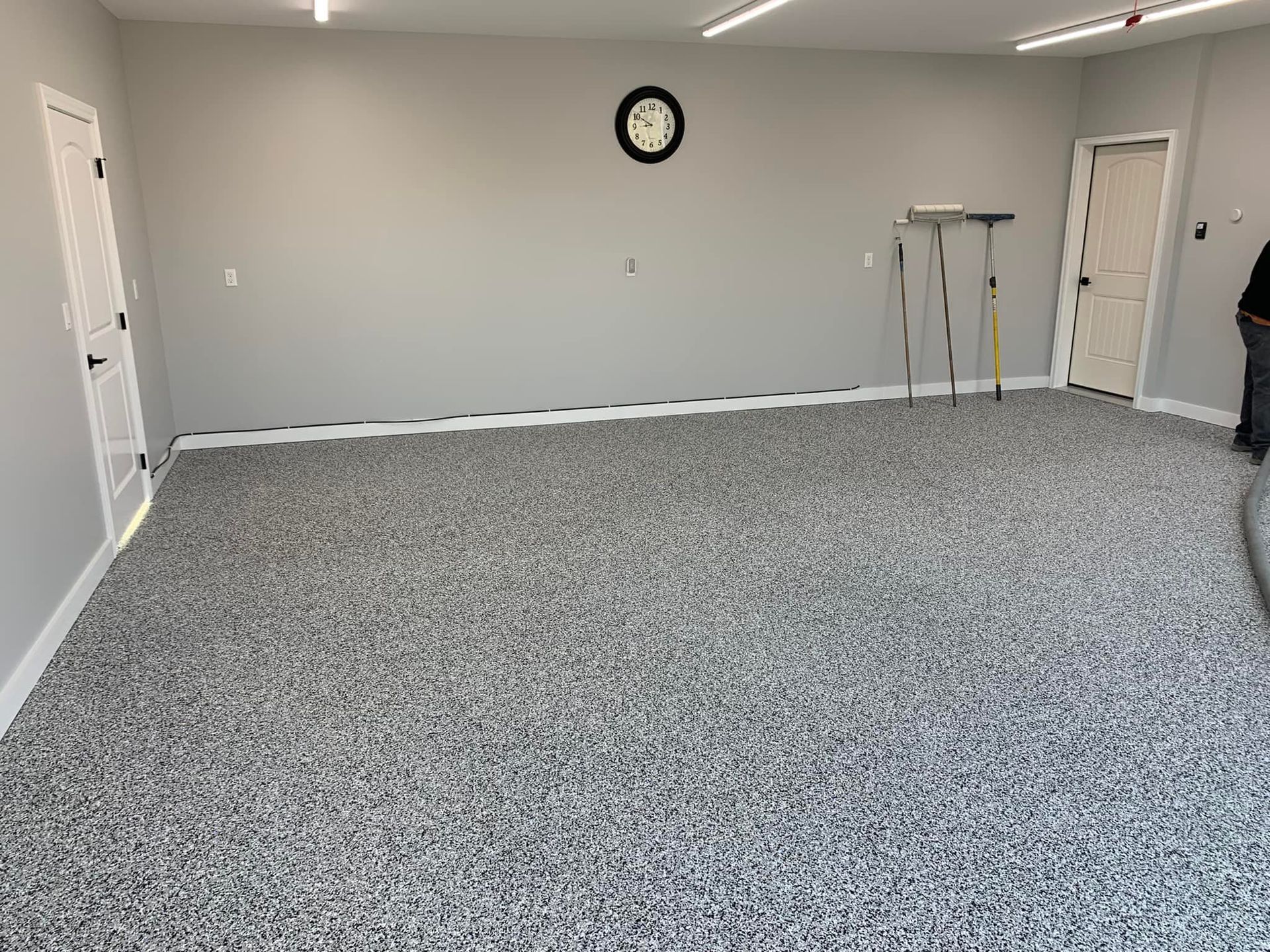 Empty gray carpeted room with white walls, a wall clock, and a walker near the back wall.