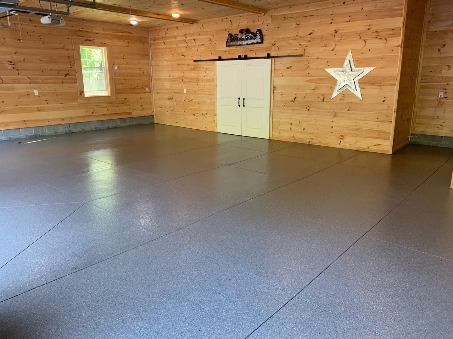 Empty wooden room with gray floor, white double doors, and a hanging star decoration.