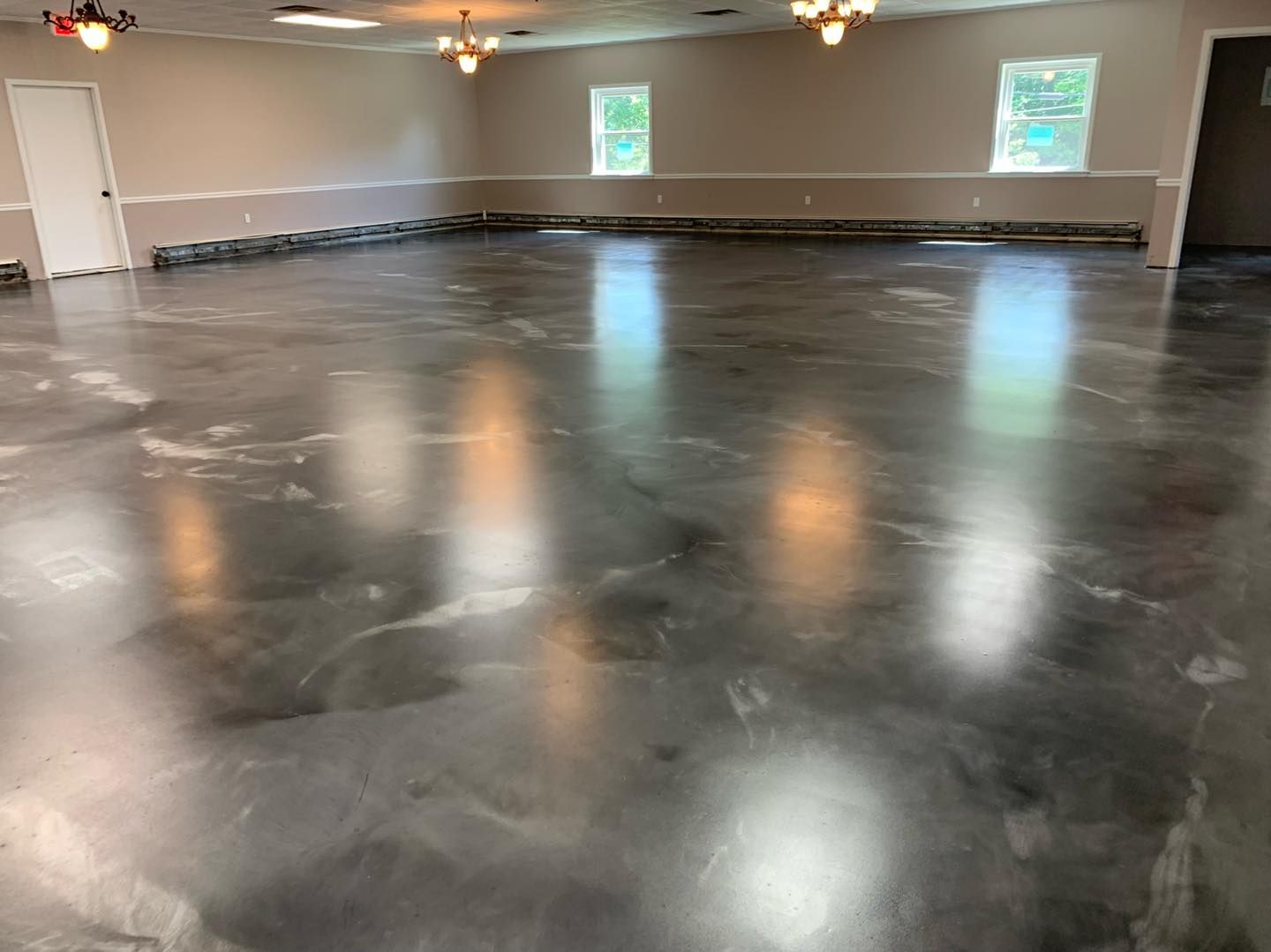 Empty room with polished dark concrete floor, white walls, and small windows at the back