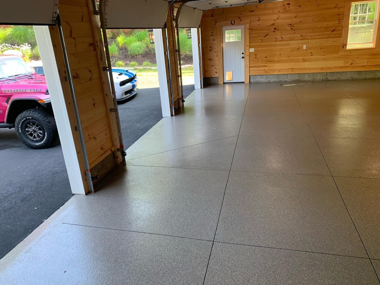 Wood-paneled covered porch with concrete floor, open doorway, and parked vehicles outside