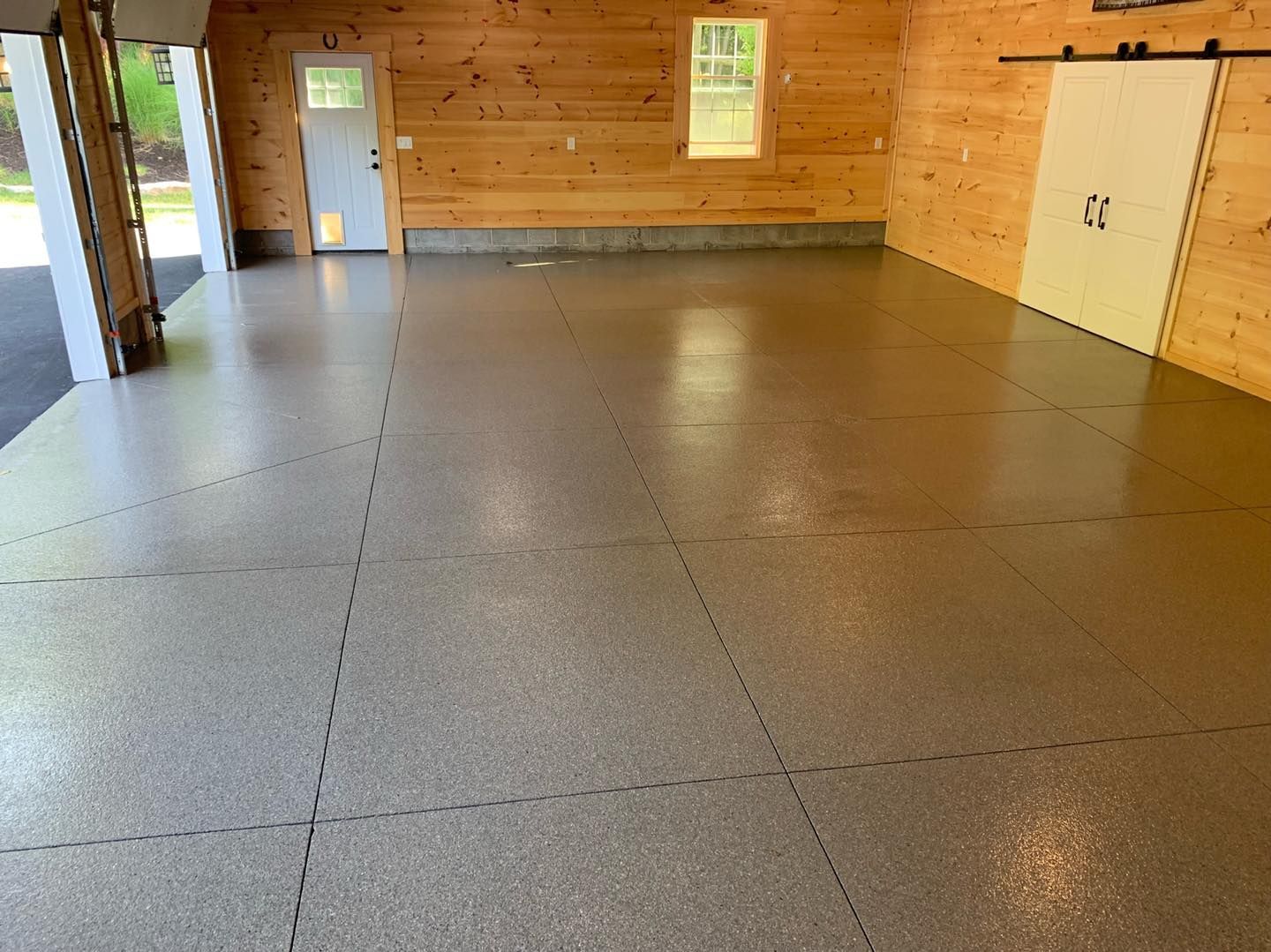 Empty wooden room with gray speckled floor and windows on the far wall
