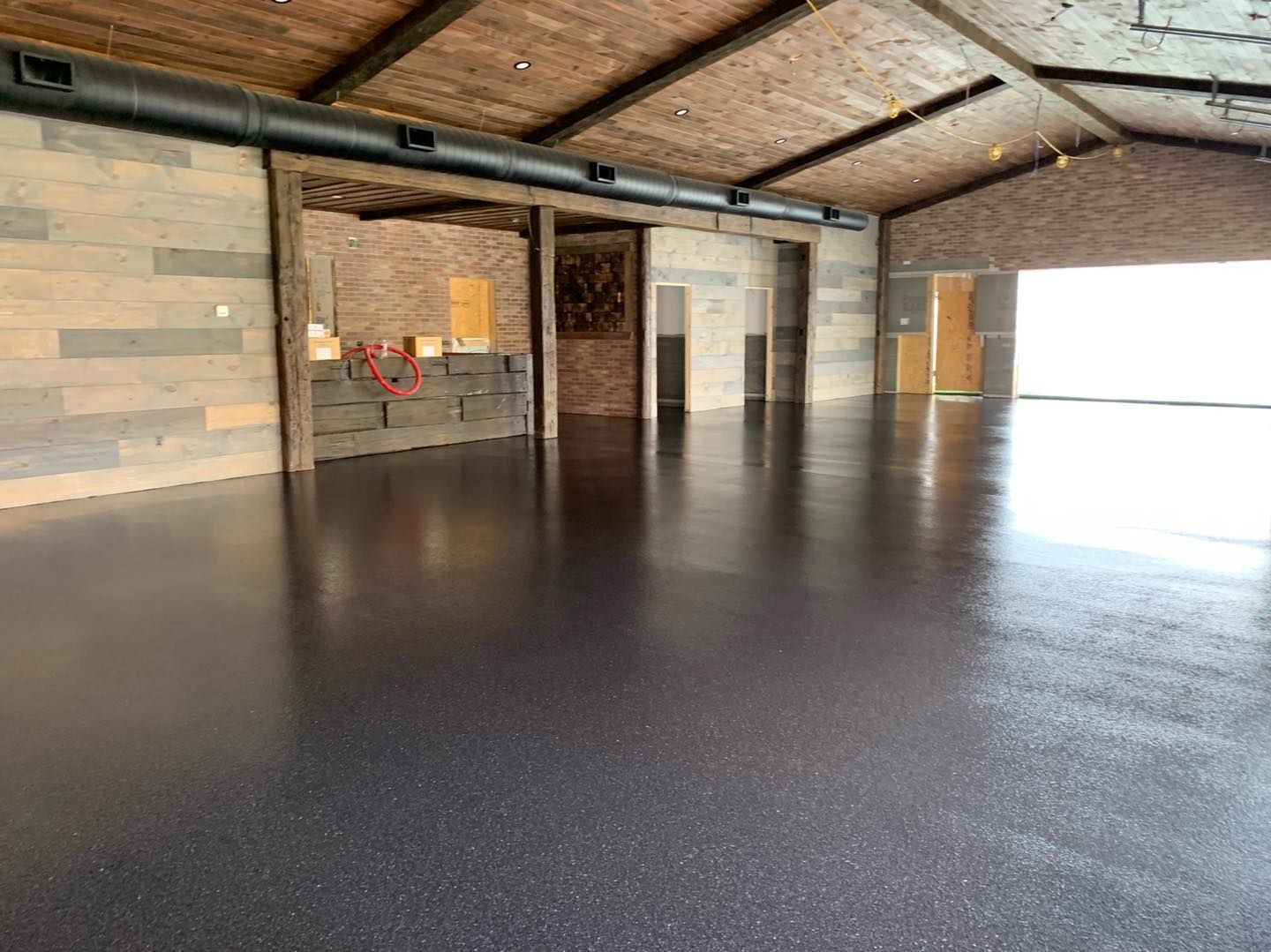Empty covered patio with stone walls, wood ceiling, and a glossy dark floor, open to bright light on one side