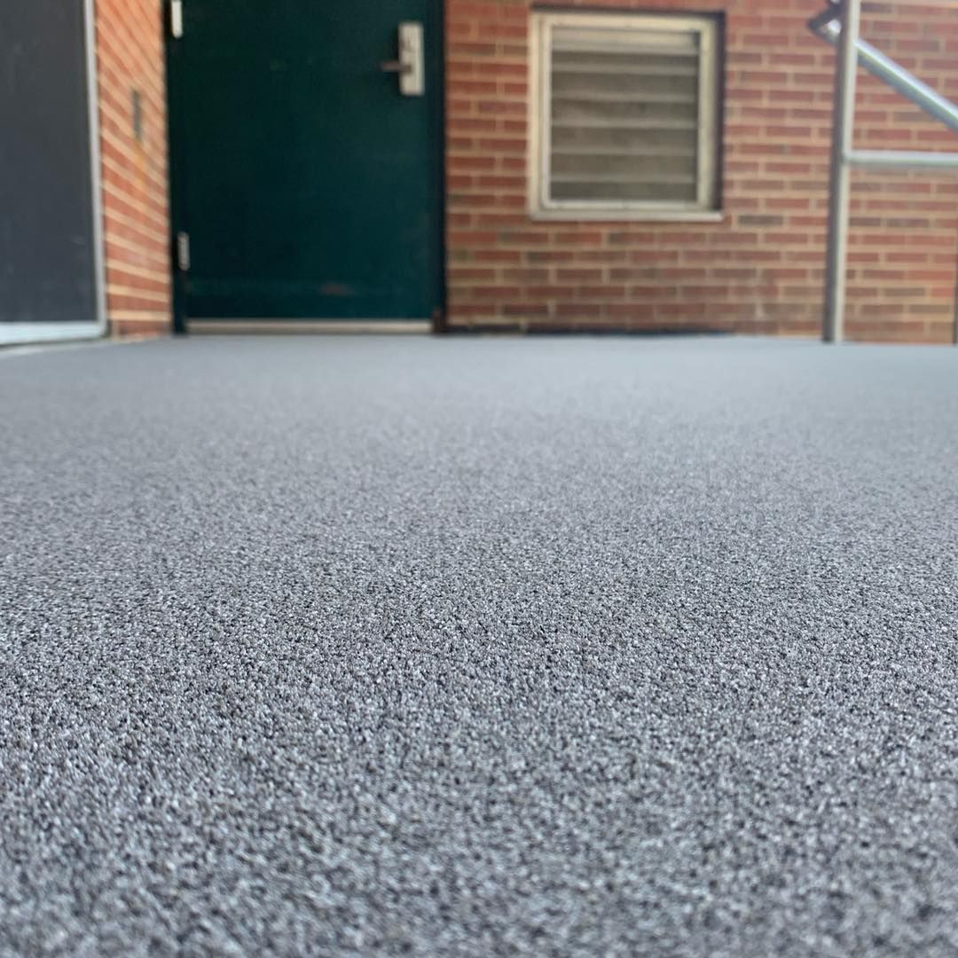 Low-angle view of a brick building entrance with a dark green door and a window on gray carpet-like ground