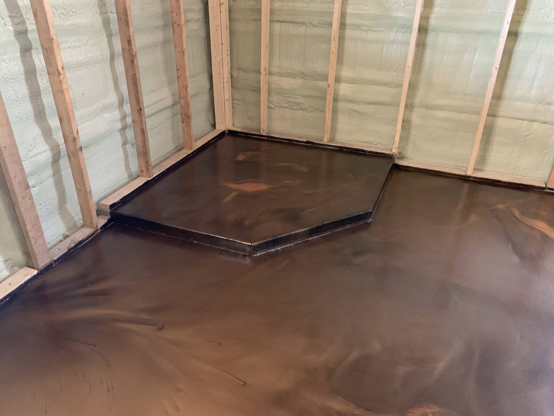 Empty room with black floor liner and a raised black platform in the corner, framed by unfinished walls.
