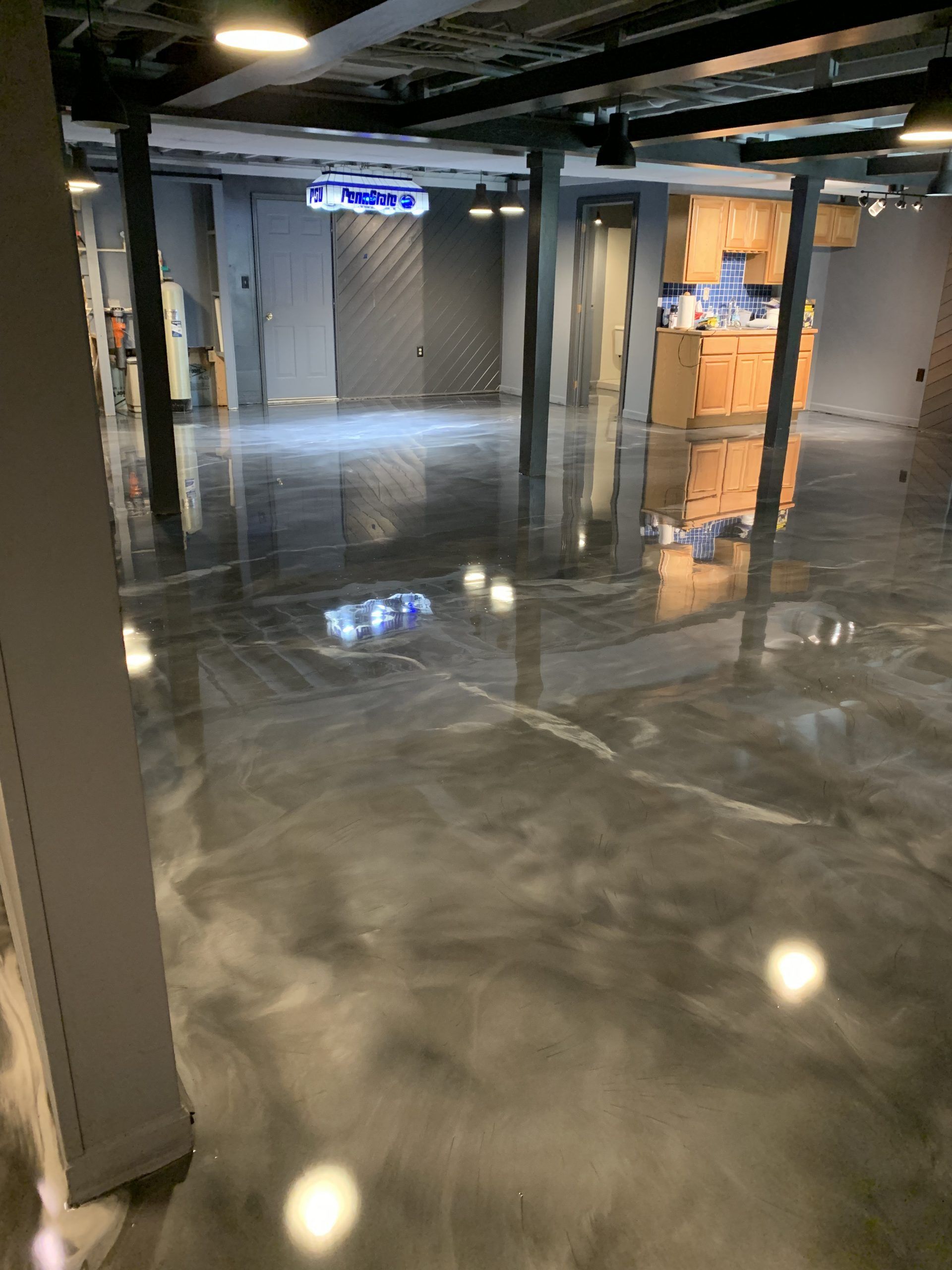 Shiny concrete lobby with black columns, gray walls, and warm-lit doorway in the background