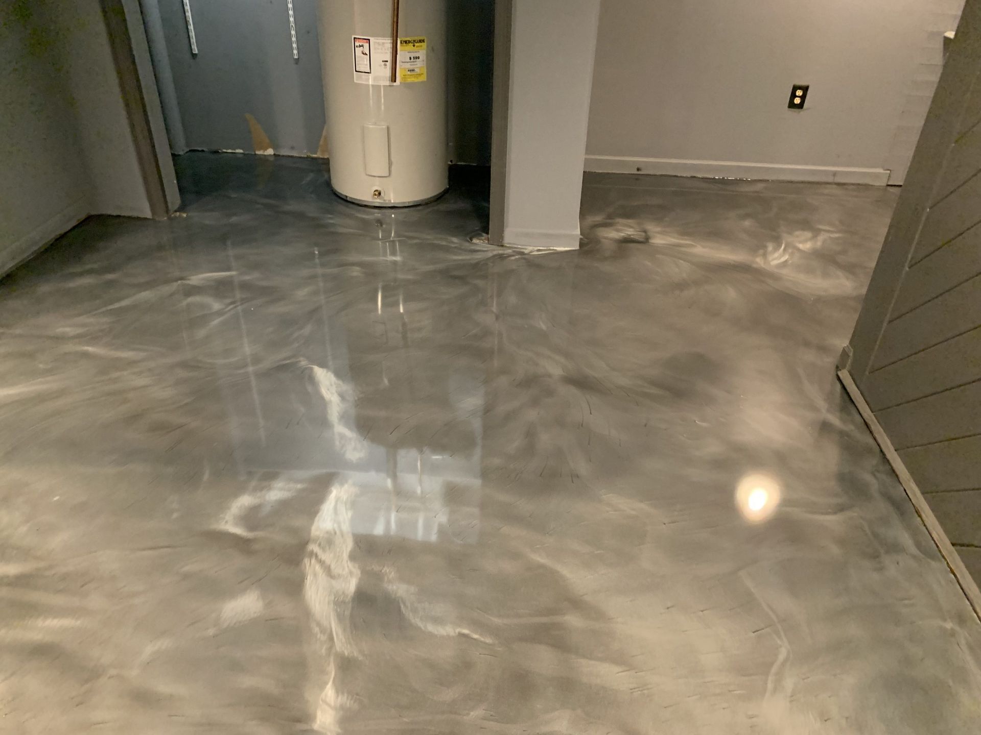 Shiny gray epoxy floor in a basement or utility room with a water heater and wall column.
