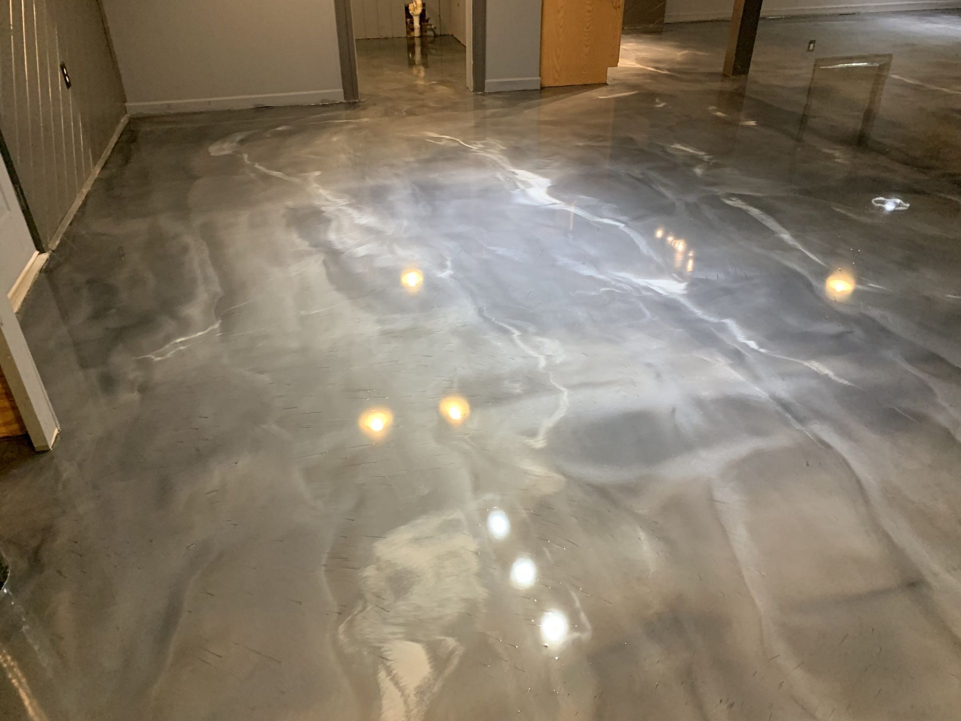 Glossy gray polished concrete floor reflecting lights in a hallway and doorway area