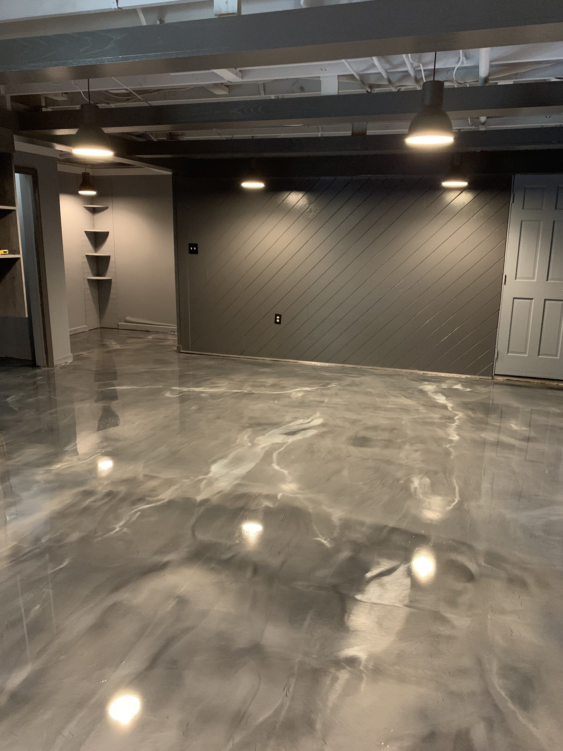 Empty industrial-style room with polished concrete floor, gray walls, and overhead lights