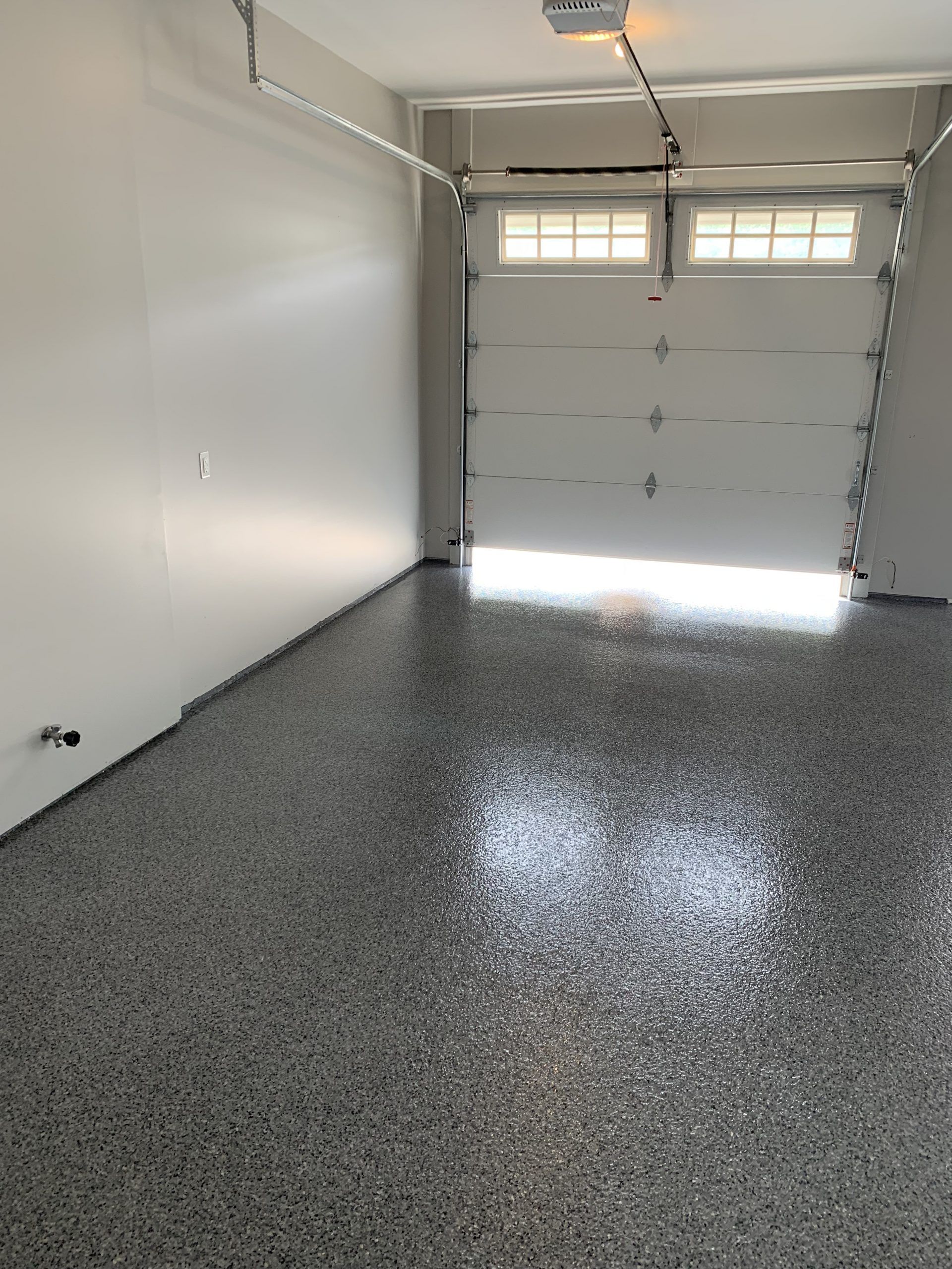 Empty garage with gray speckled floor and closed white door, lit by daylight.