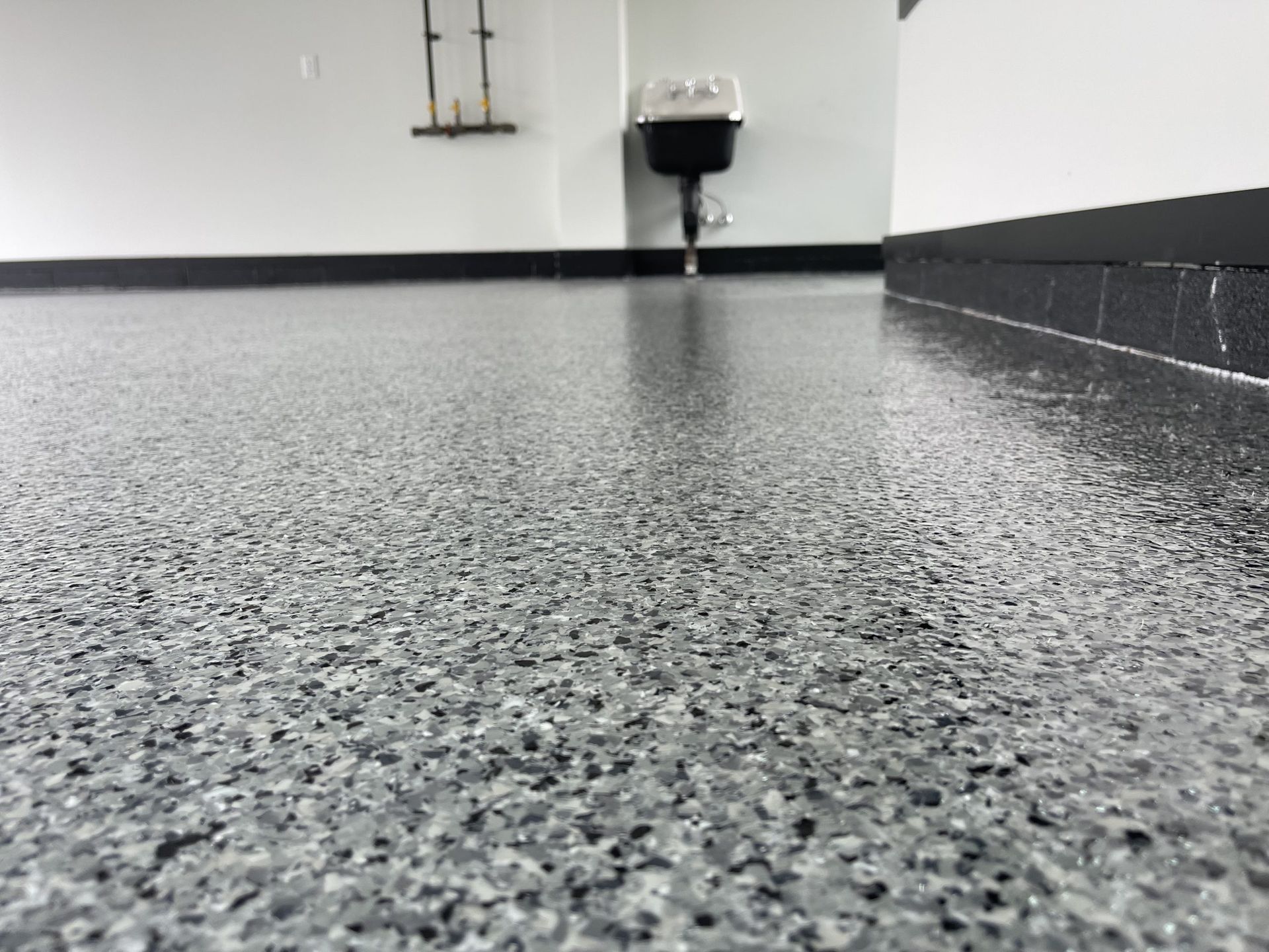Empty room with speckled gray floor and wall-mounted sink in the back corner
