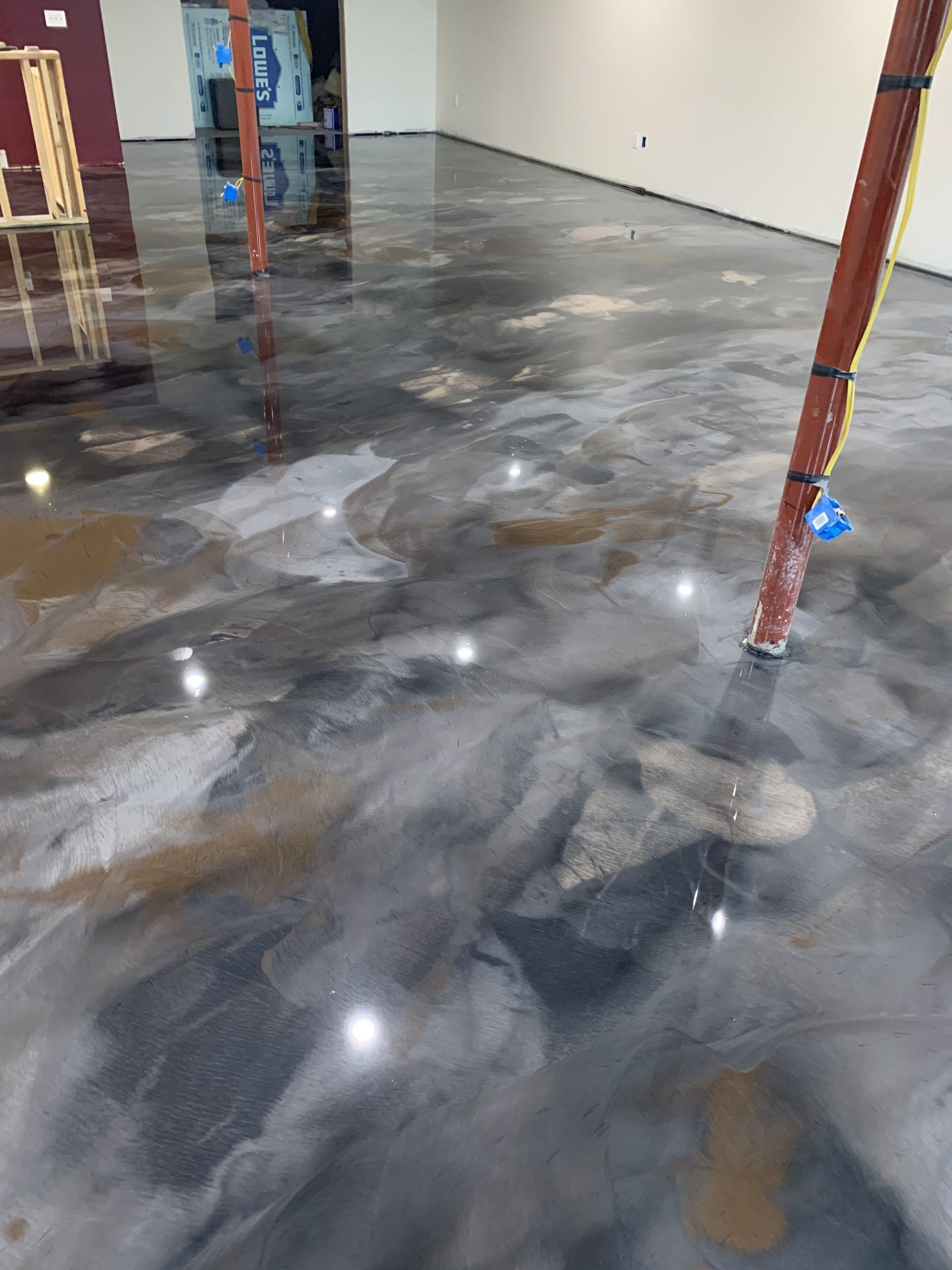 Shiny dark concrete floor in an unfinished interior space with red columns and a white wall
