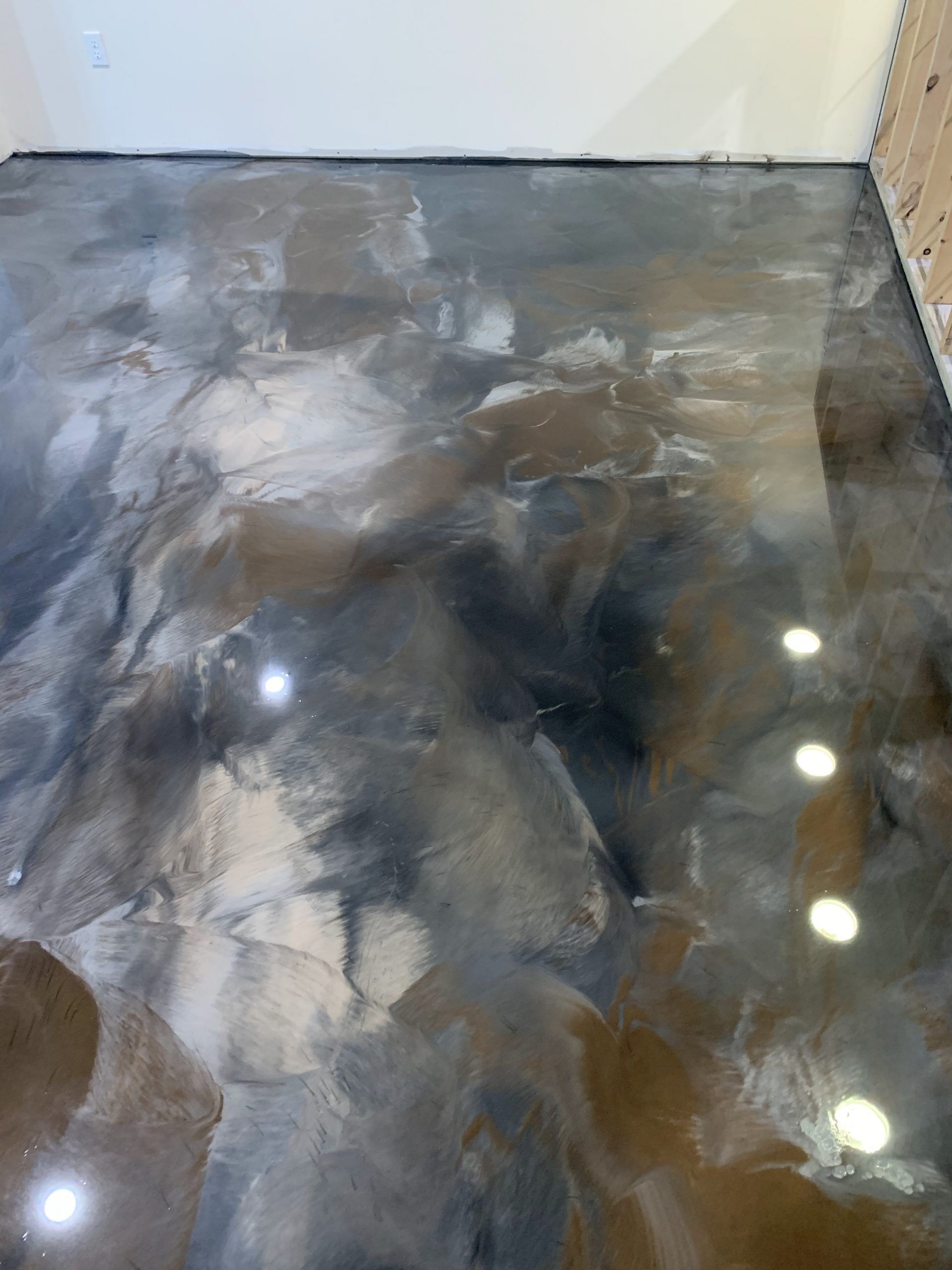Shiny gray-and-black marble floor in a small room, with reflected lights and unfinished edges