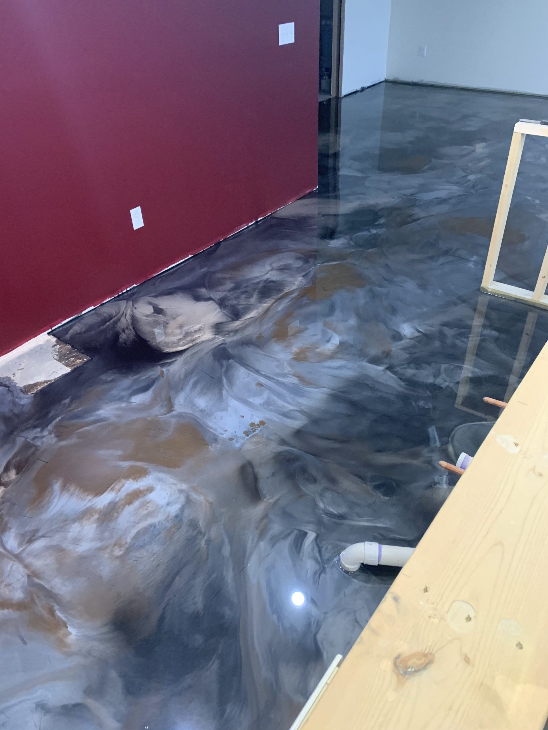 Interior floor with water and mud damage beside a red wall and wooden railing.