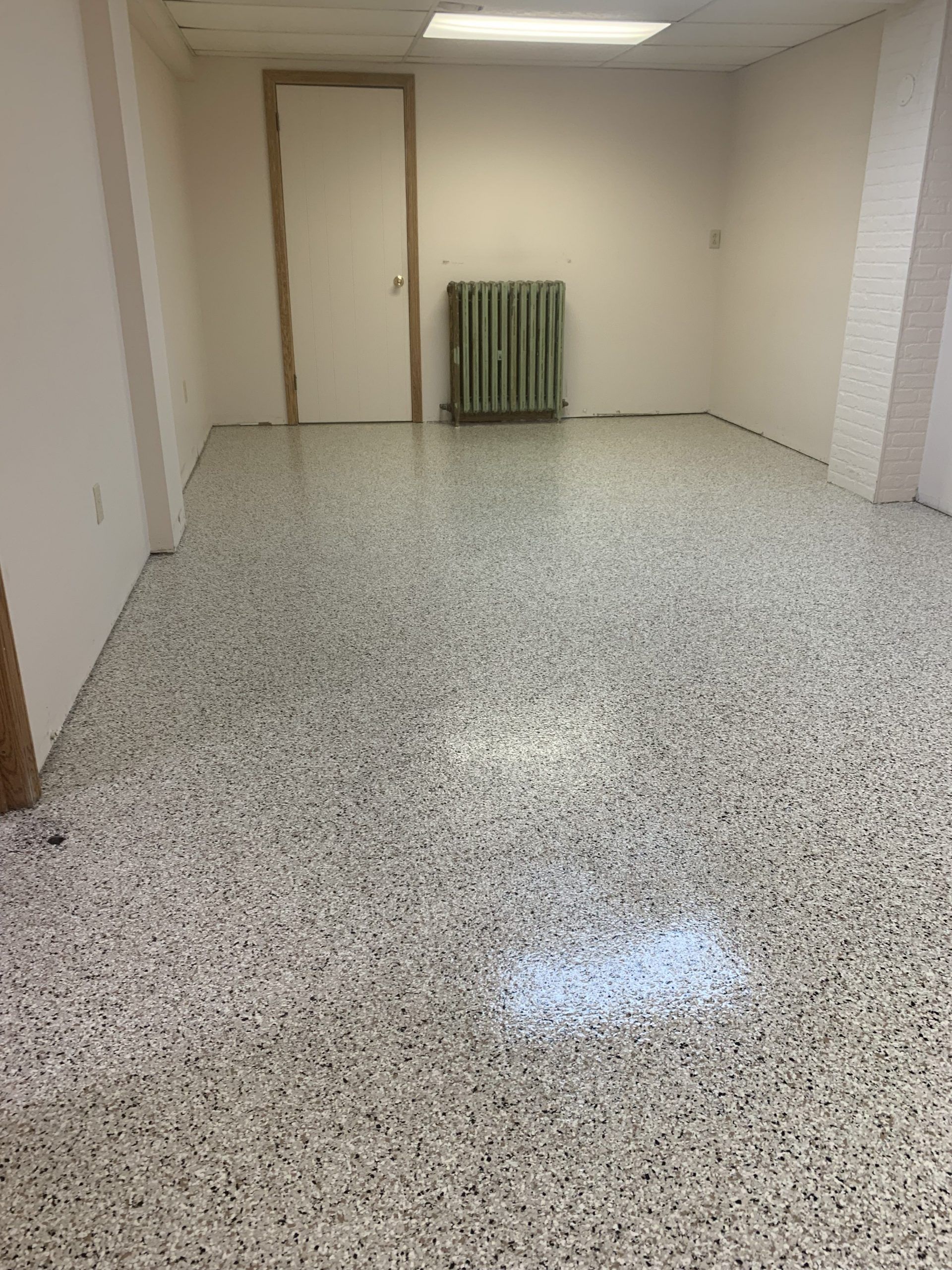 Empty beige room with speckled floor and a radiator against the back wall