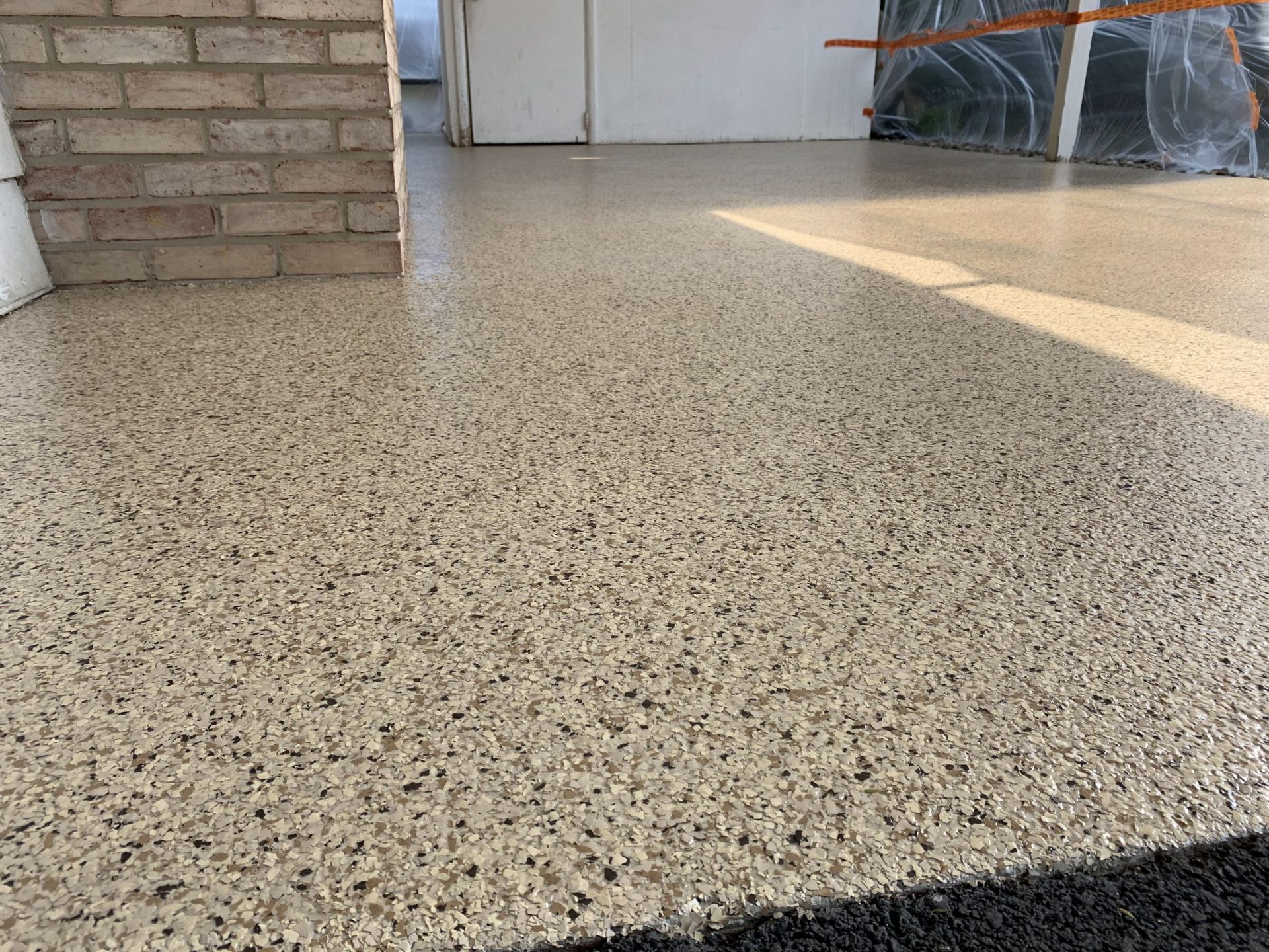 Speckled concrete floor beside a brick wall and sunlit doorway area