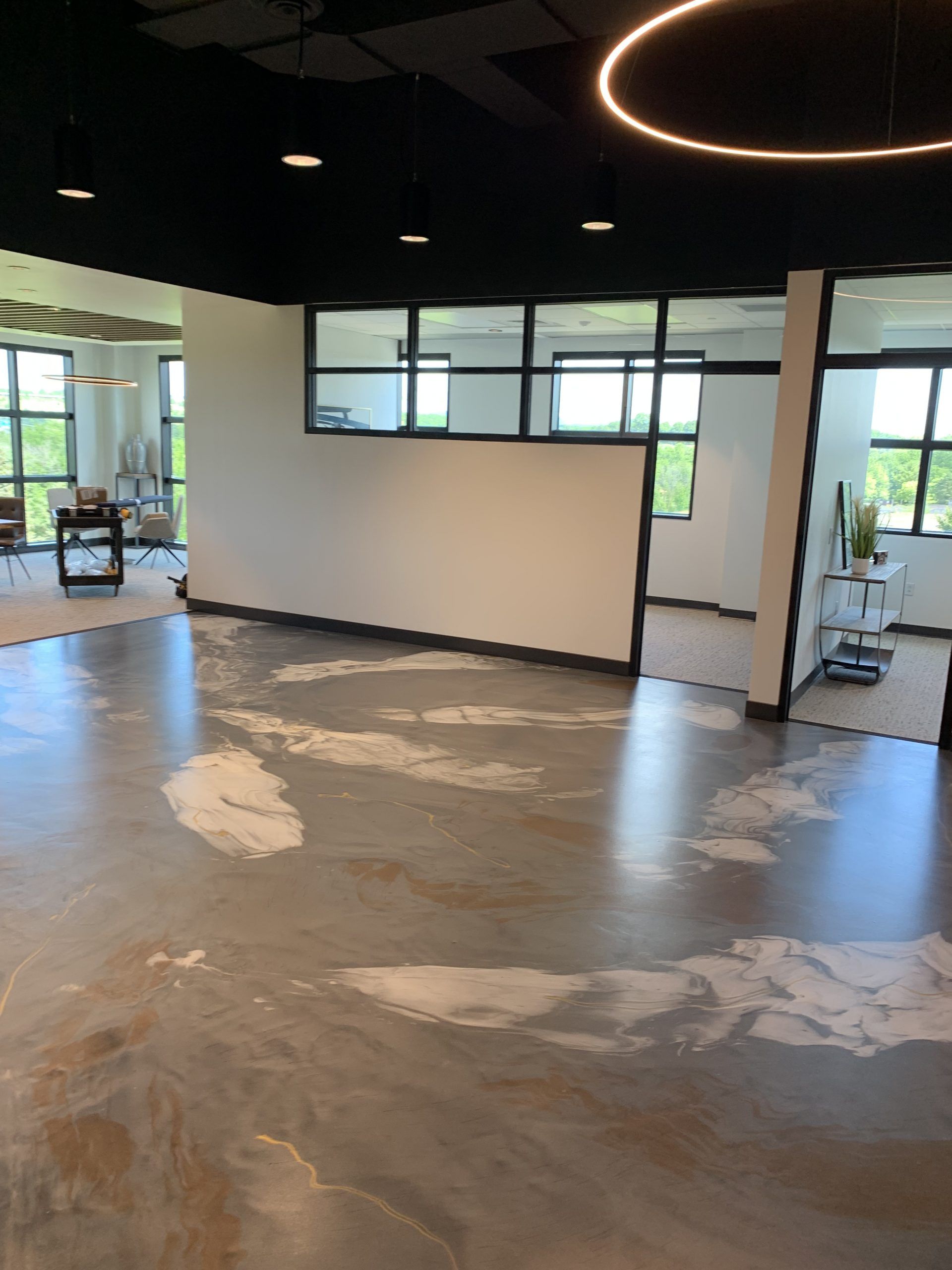 Empty modern office space with concrete floor, white walls, black ceiling, and large windows.