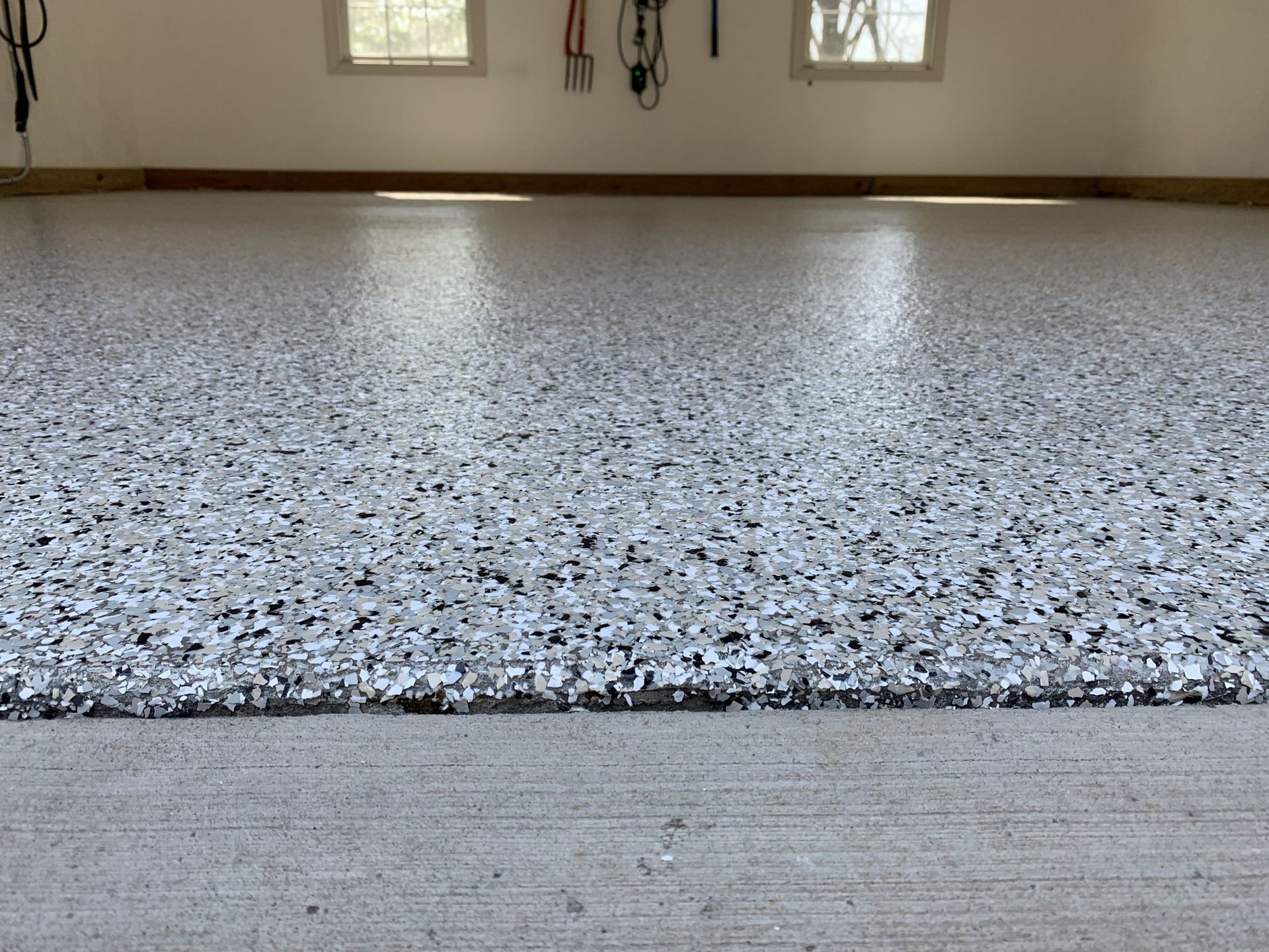 Close-up of a speckled epoxy floor in an empty room with windows and baseboards along the wall.