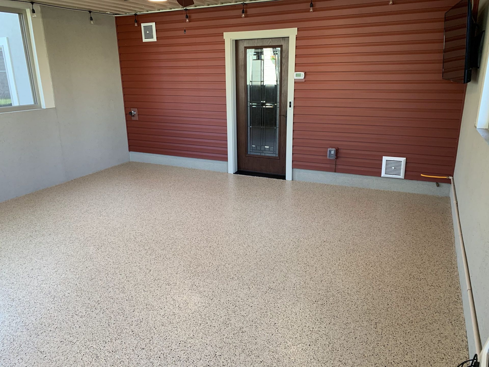 Empty covered patio with beige floor, red wood-paneled wall, and a glass door centered on the back wall
