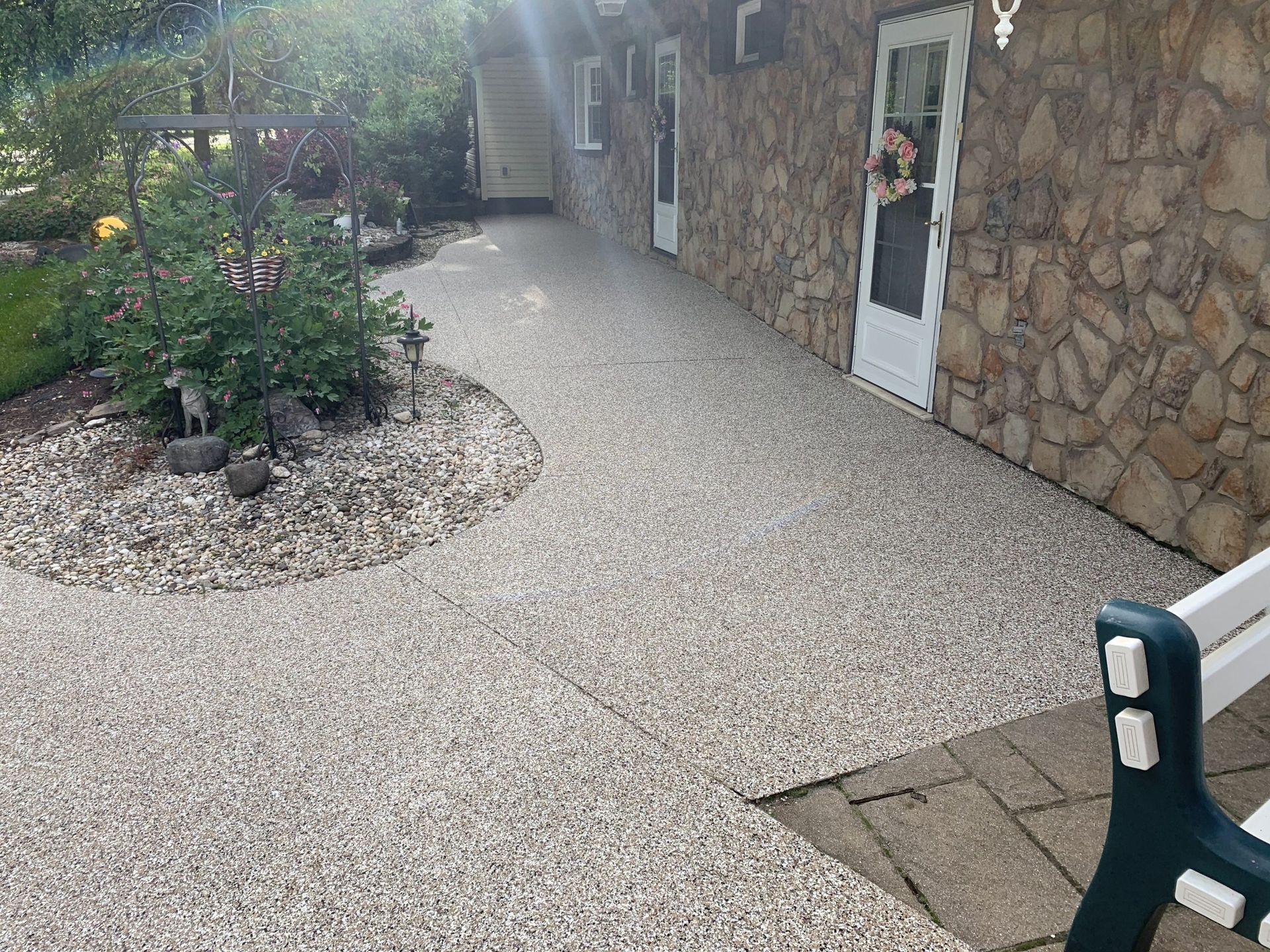 Gravel courtyard beside a stone building with a door, potted plant, and patio chairs in the foreground