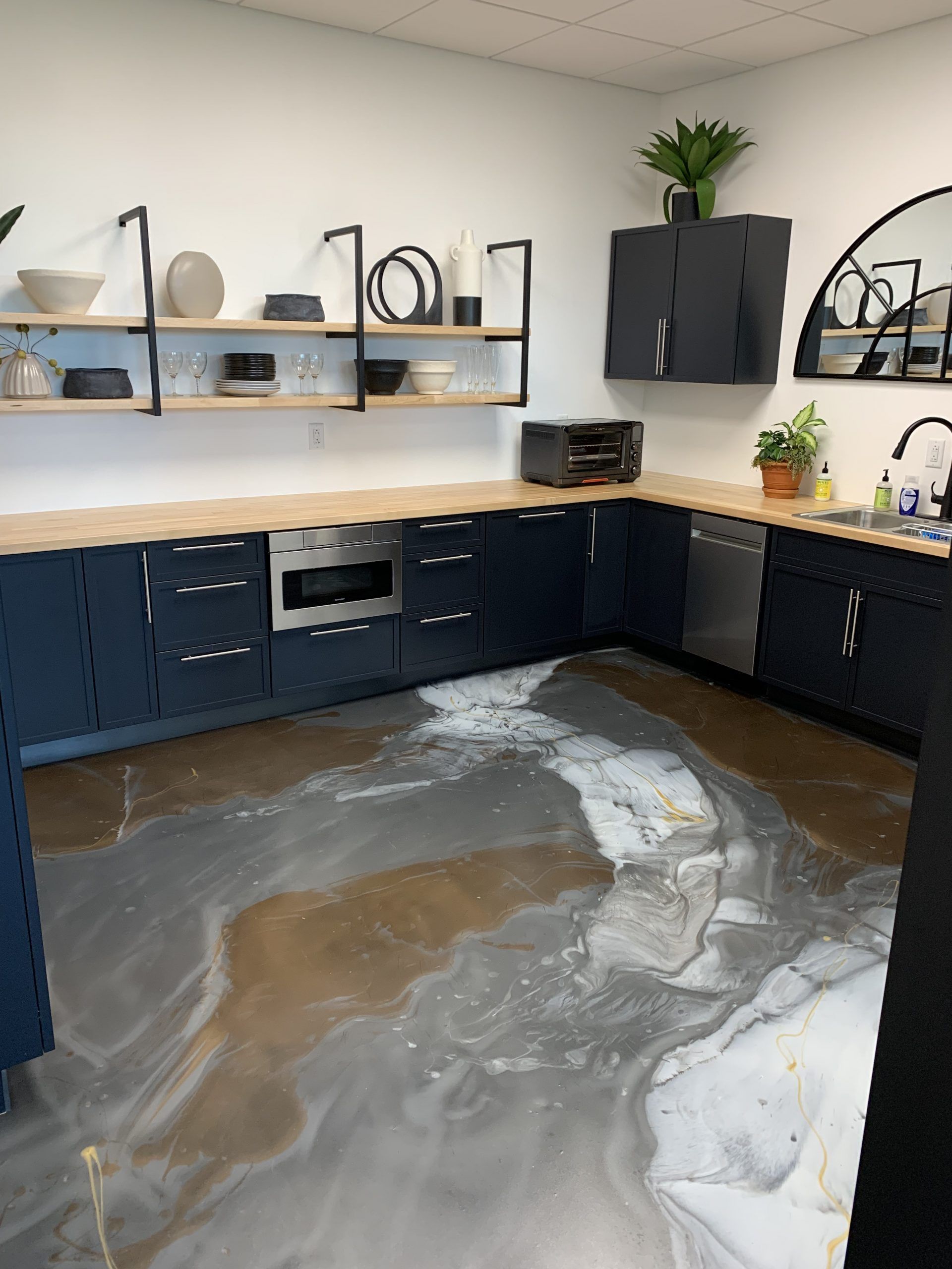 Flooded office kitchen with dark cabinets, wet gray floor, and water pooled across the room