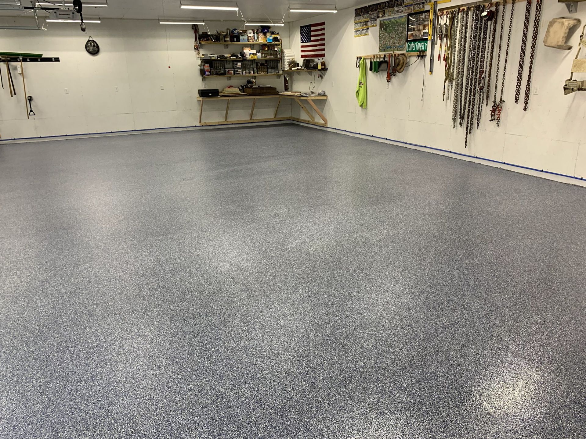 Empty garage with gray speckled floor, wall-mounted tools, shelves, and an American flag.