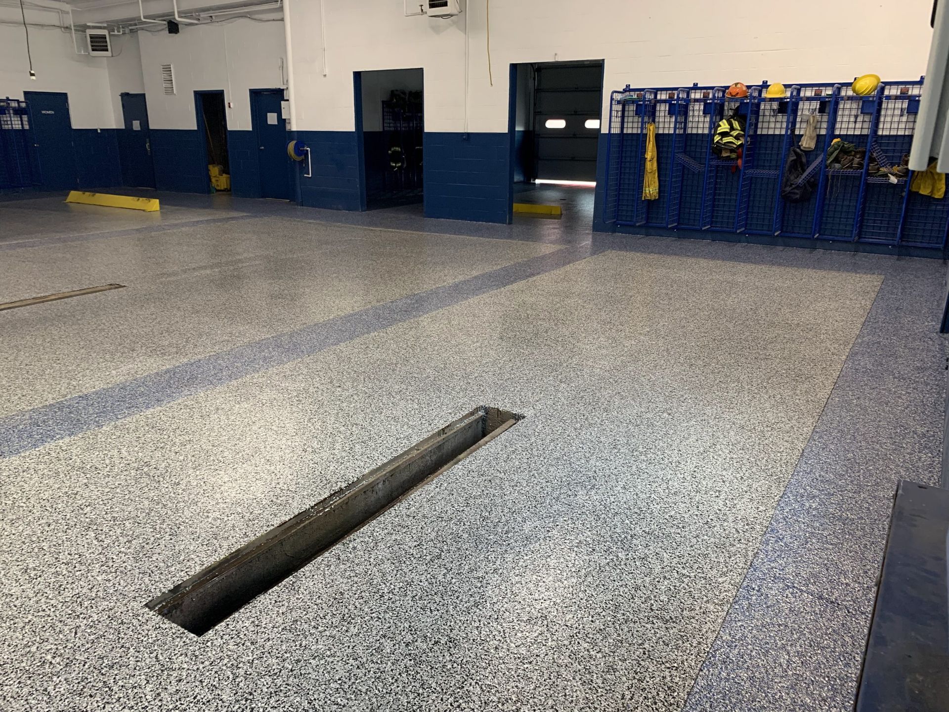 Auto shop floor with a long rectangular service pit and blue tool racks against the wall