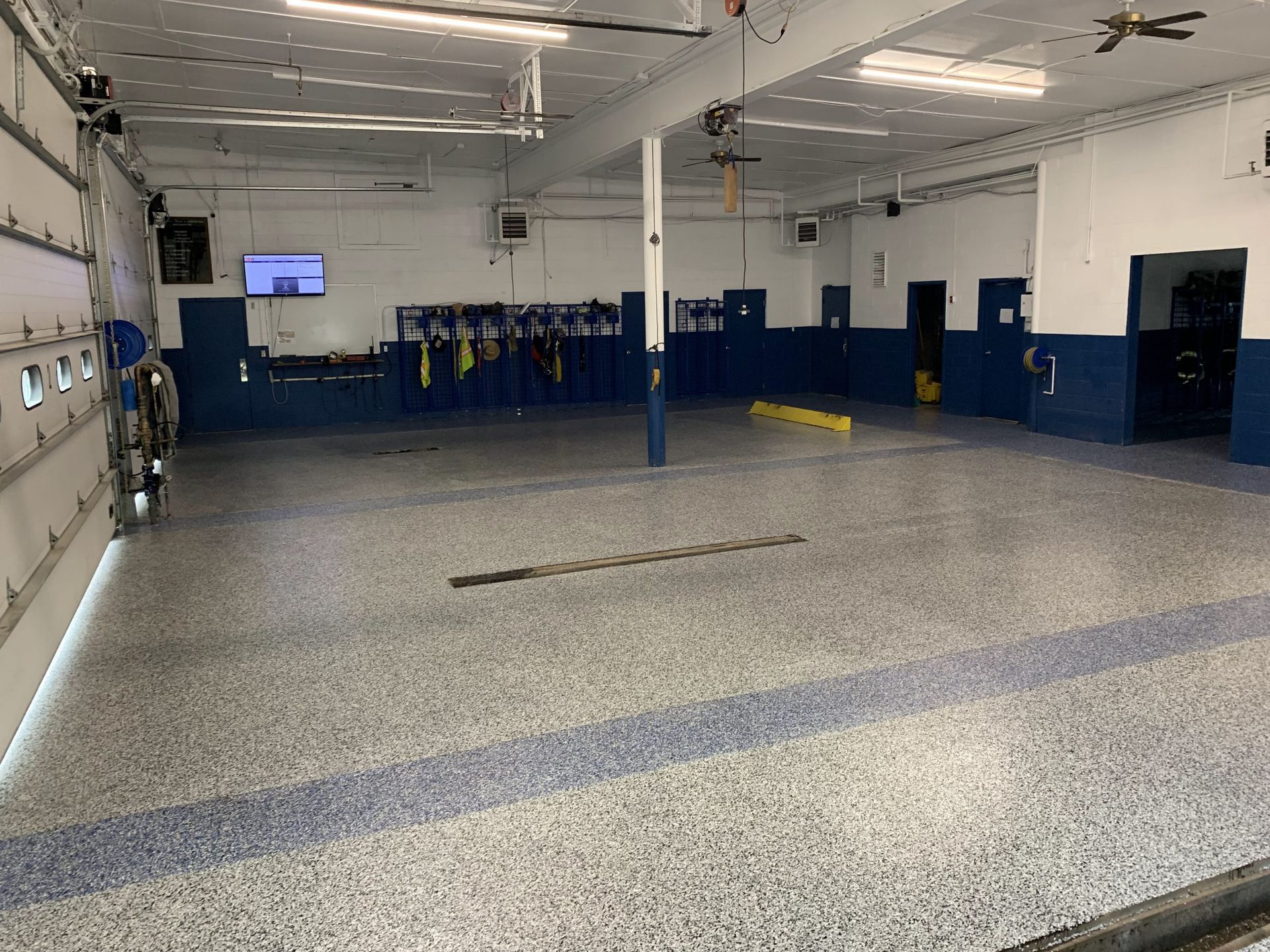 Empty auto shop with blue walls, lifts, and a gray speckled floor under fluorescent lights