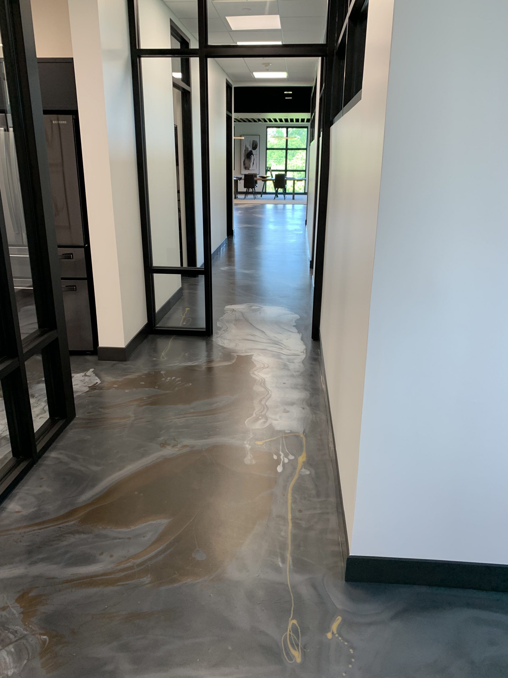 Long hallway with glossy concrete floor, black-framed glass doors, and white walls