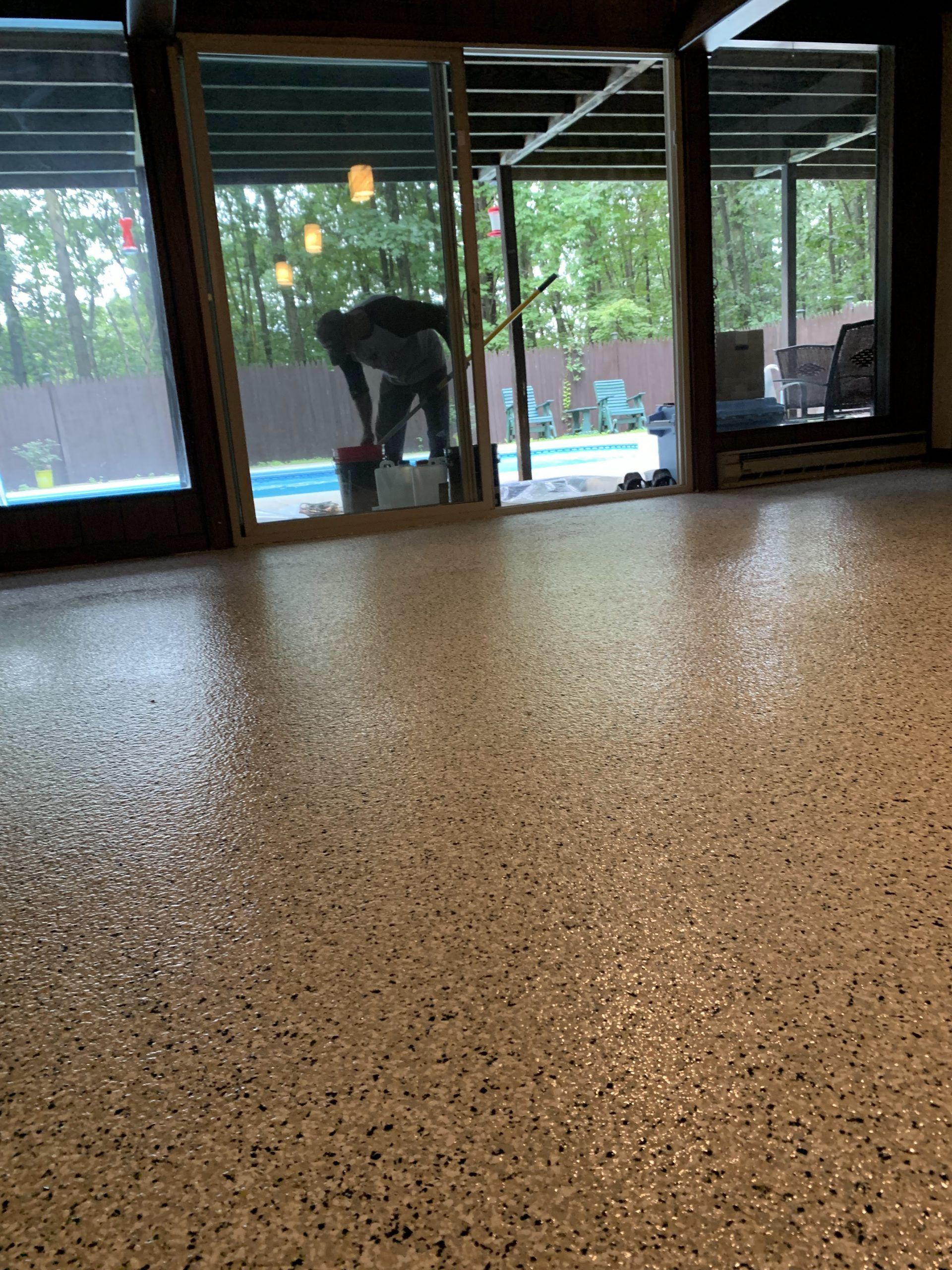 Indoor room with speckled floor and large windows; a person bends near the back wall.