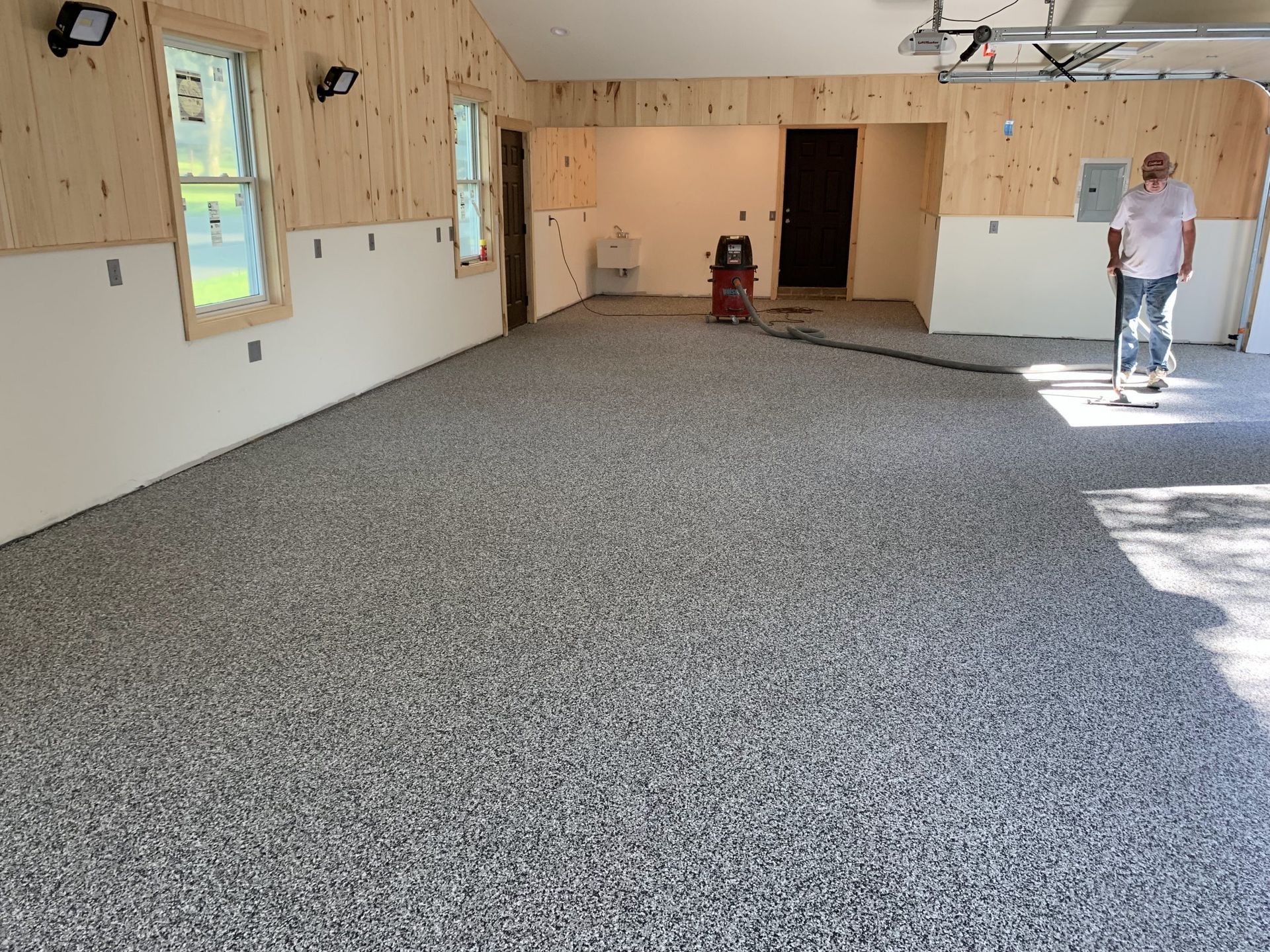 Carpeted room with wood-paneled walls, windows, and a person standing near the right wall.