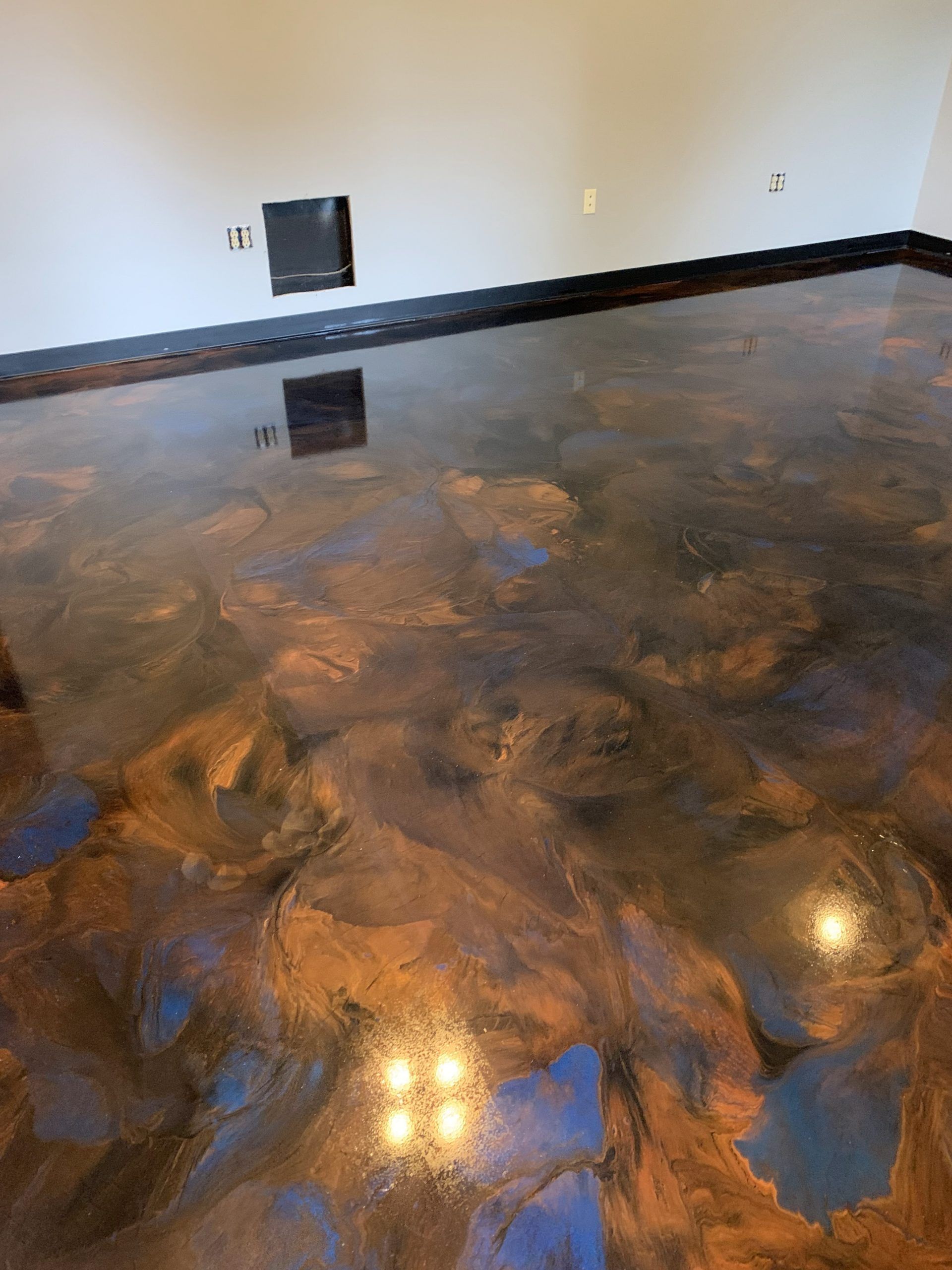 Glossy brown and blue metallic epoxy floor in an empty room with white walls and outlets