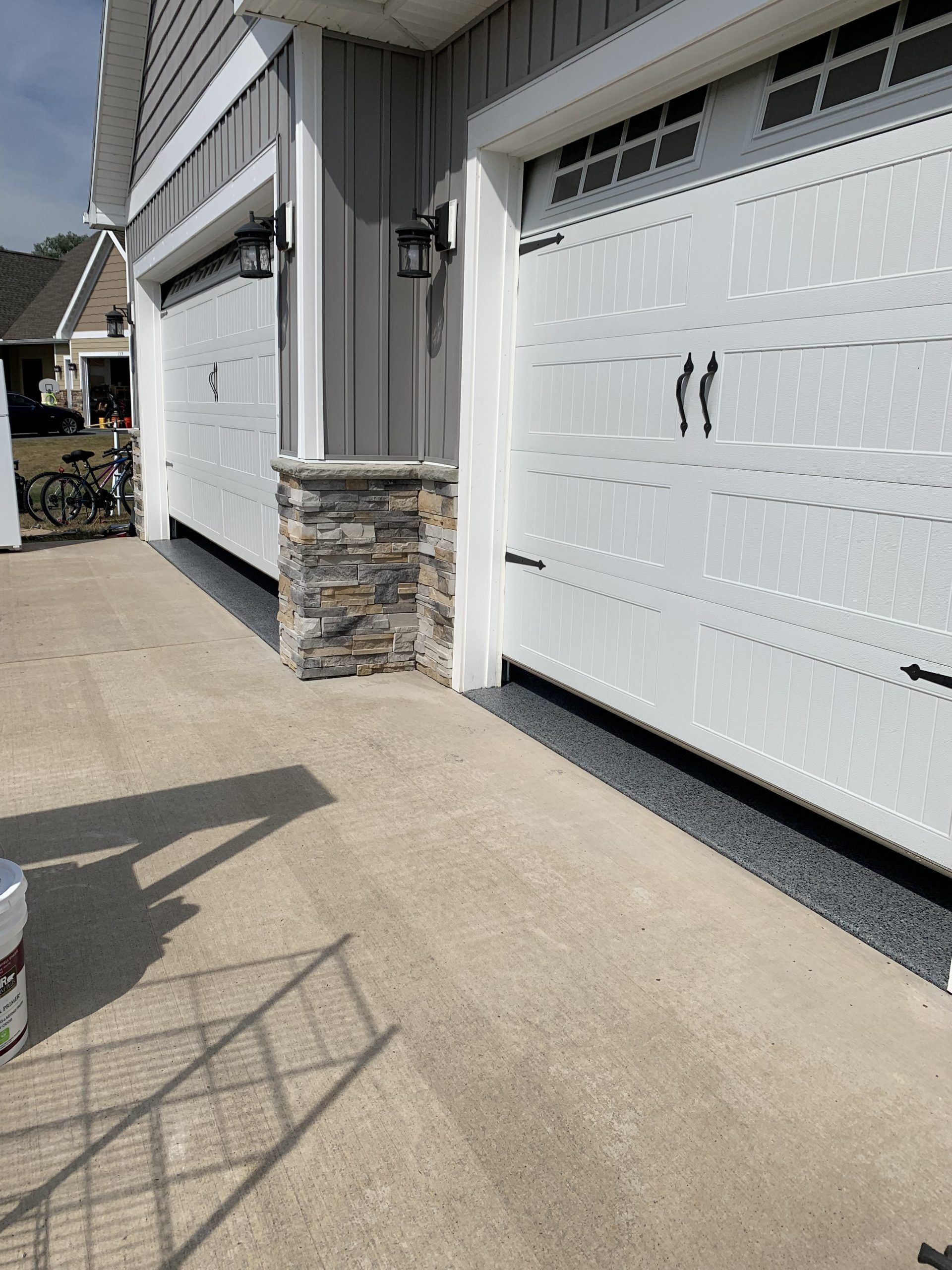 Two white garage doors on a gray house with stone columns along a concrete driveway