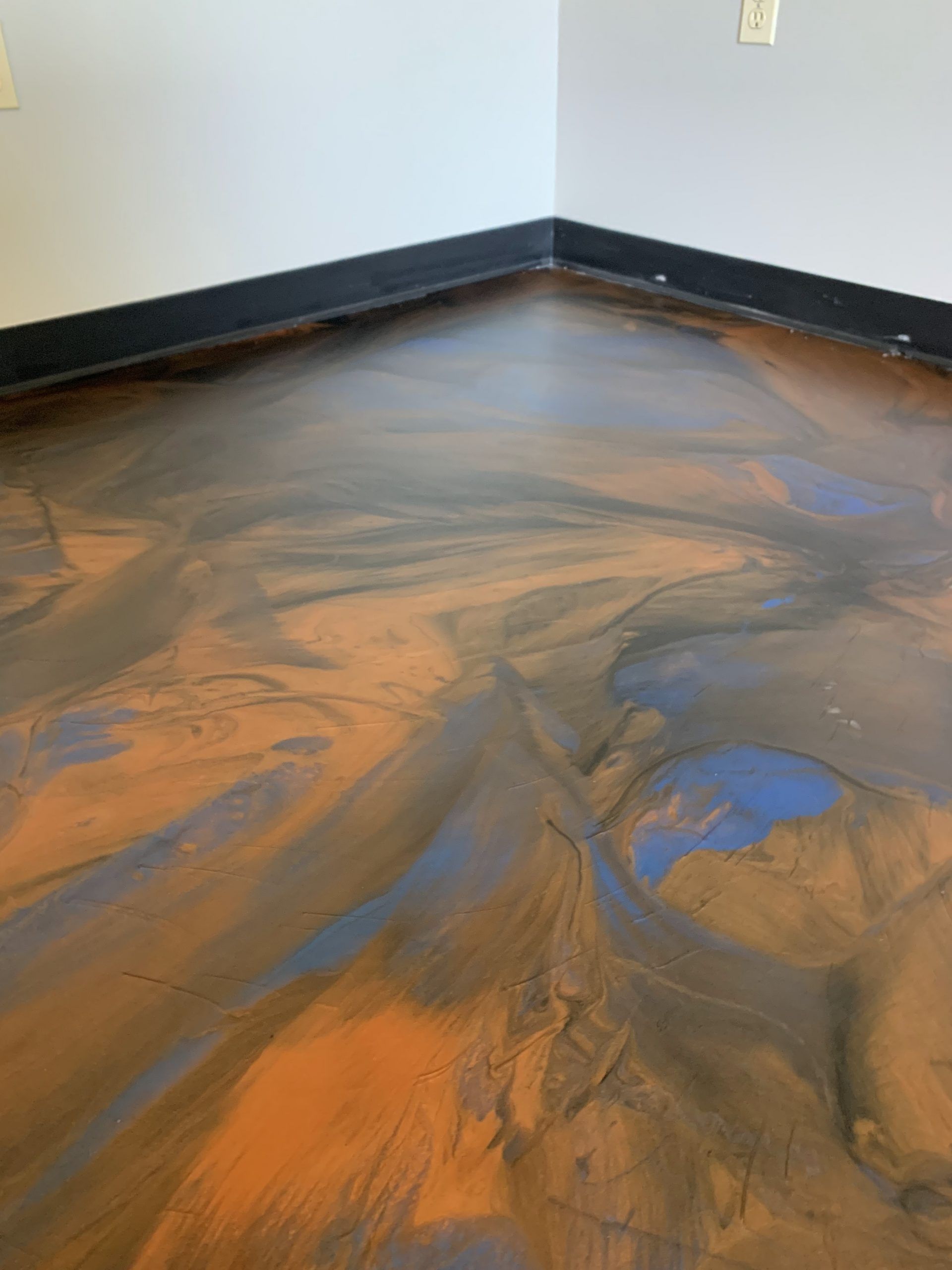 Abstract swirls of orange and blue on a floor inside a room with black baseboards.