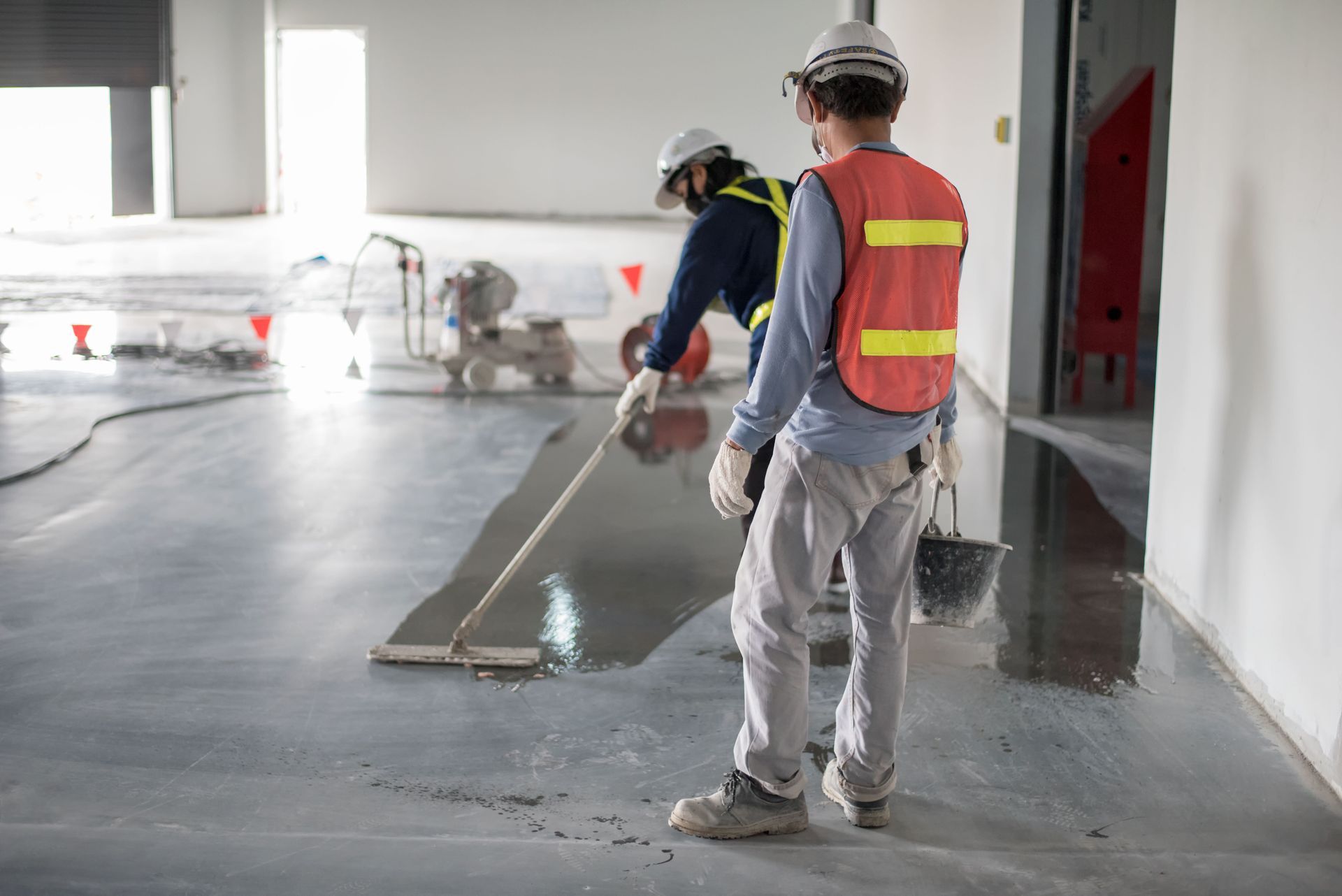 Workers smoothing wet concrete in a large indoor construction area
