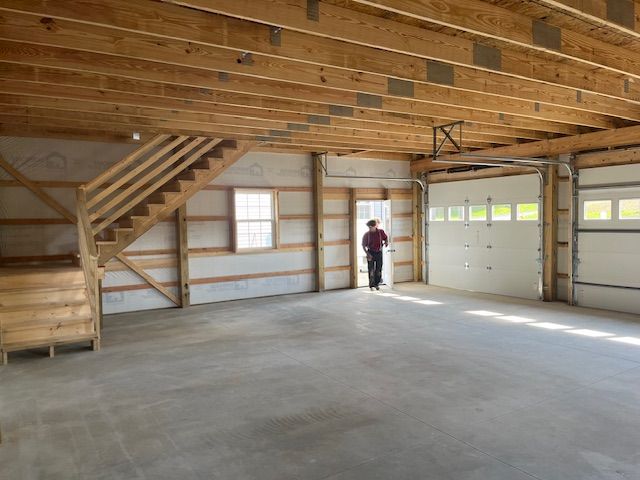 A man is standing in an empty garage with stairs and a garage door.