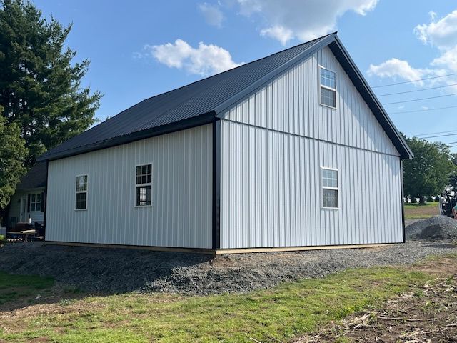 A white barn with a black roof is sitting in the middle of a grassy field.