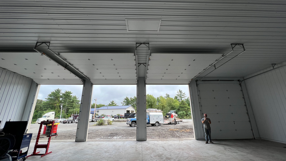 A man is standing in a garage with the doors open.