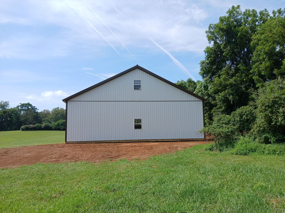 White barn on a grassy field under a blue sky with trees.