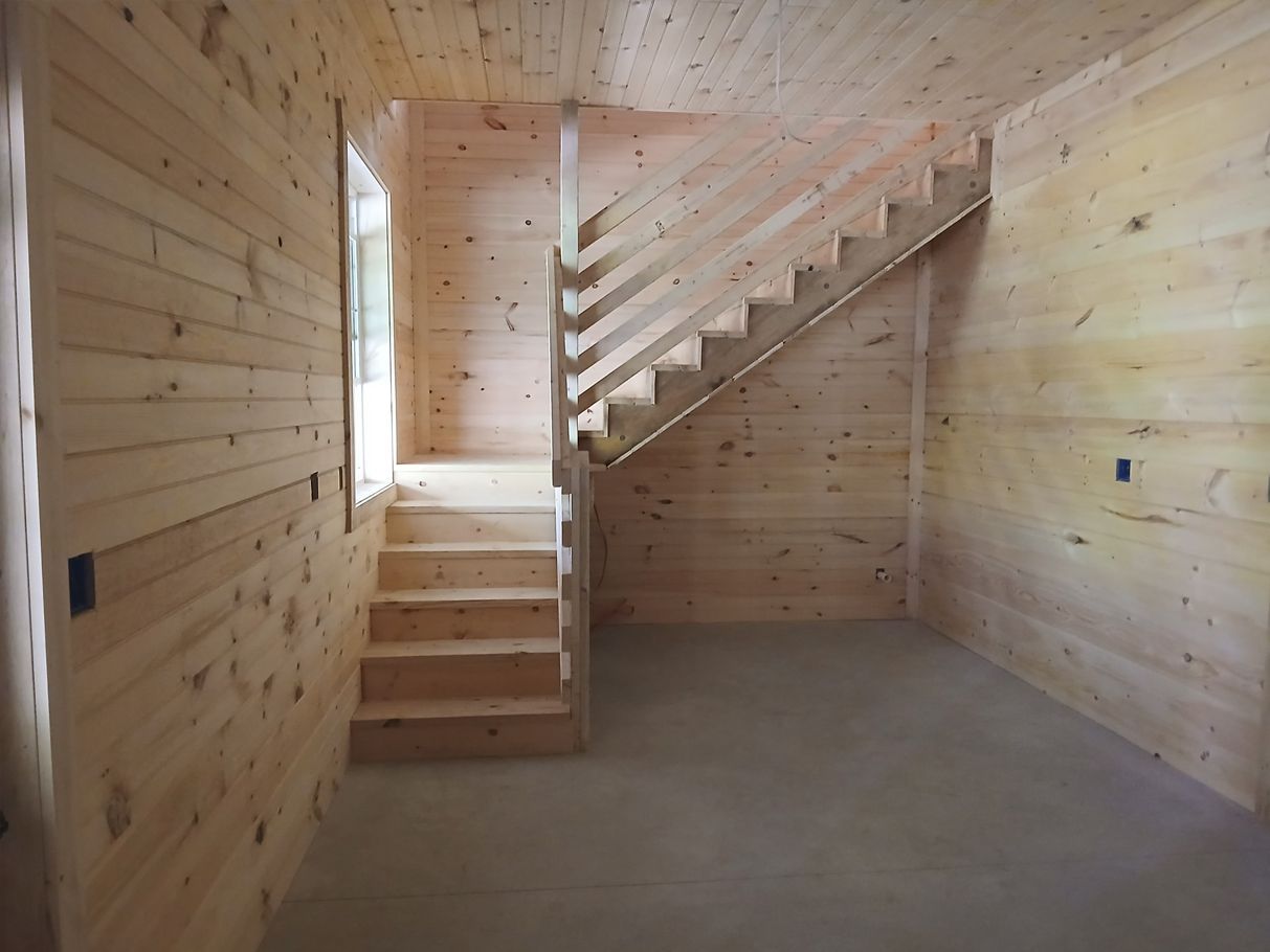 Interior of a wooden room with stairs. Wooden walls, stairs, and ceiling. Concrete floor. Sunlight through a window.