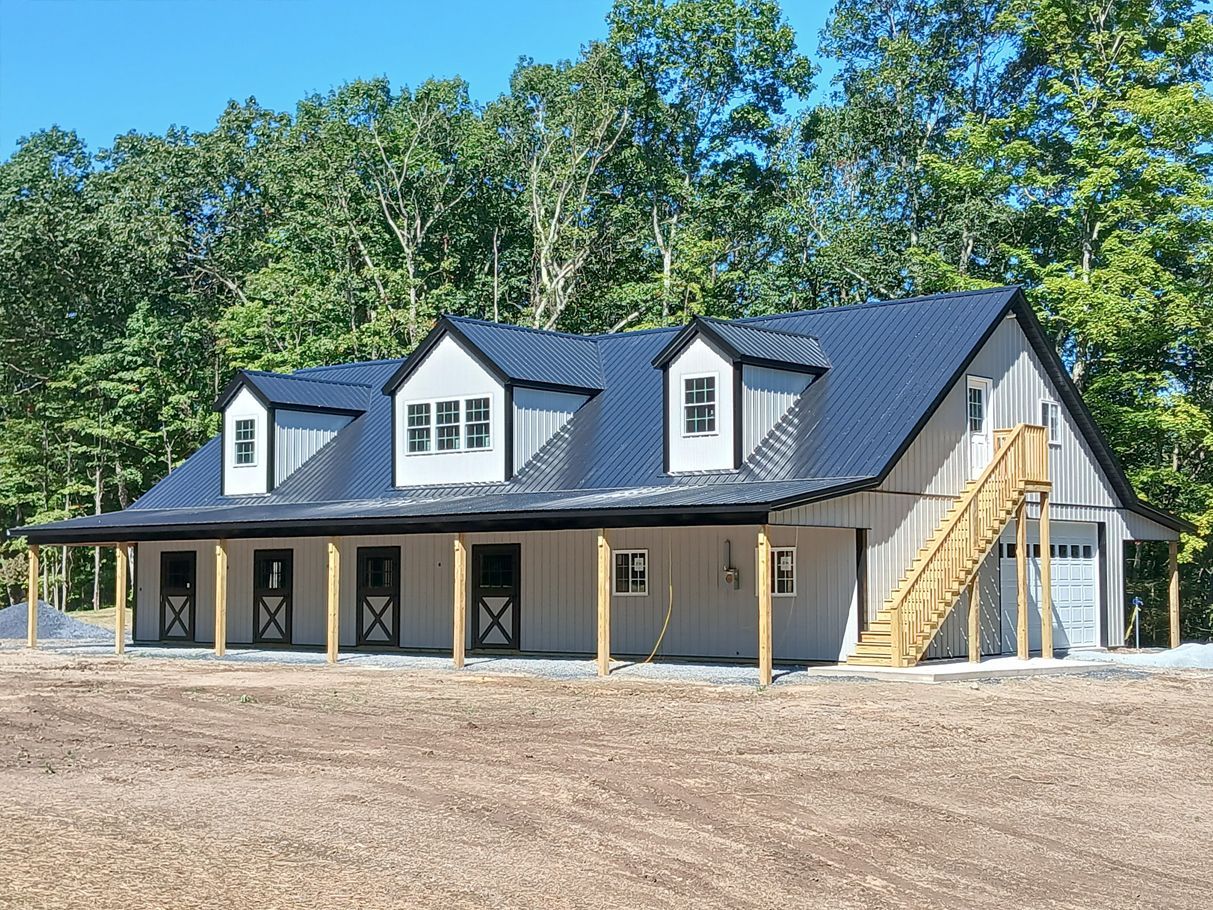 Farmhouse with dark roof, white siding, black trim, porch, and garage, set in a field with trees in the background.