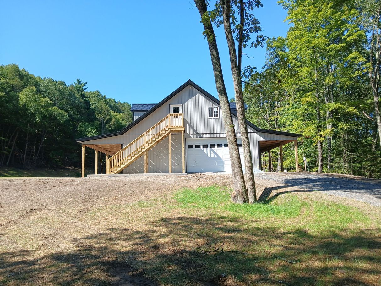 Two-story gray and white building with a garage, porch, and exterior staircase in a wooded area.