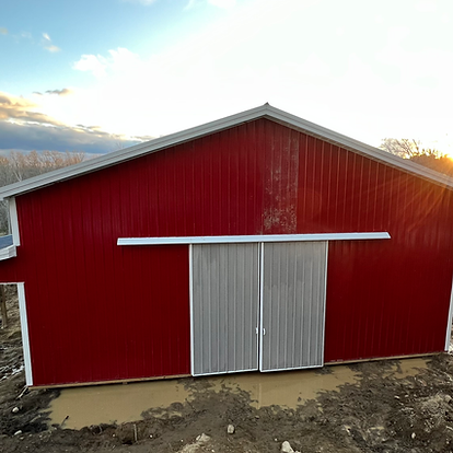 A red barn with a sliding barn door is sitting in the dirt.