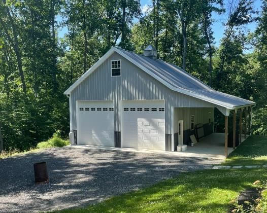 A garage with two garage doors and a porch surrounded by trees