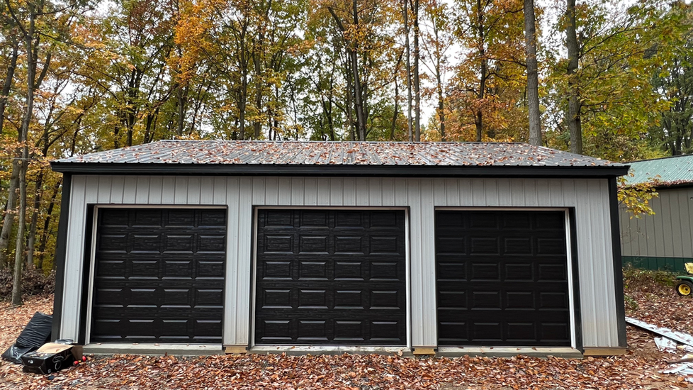 A garage with three black garage doors is surrounded by trees.
